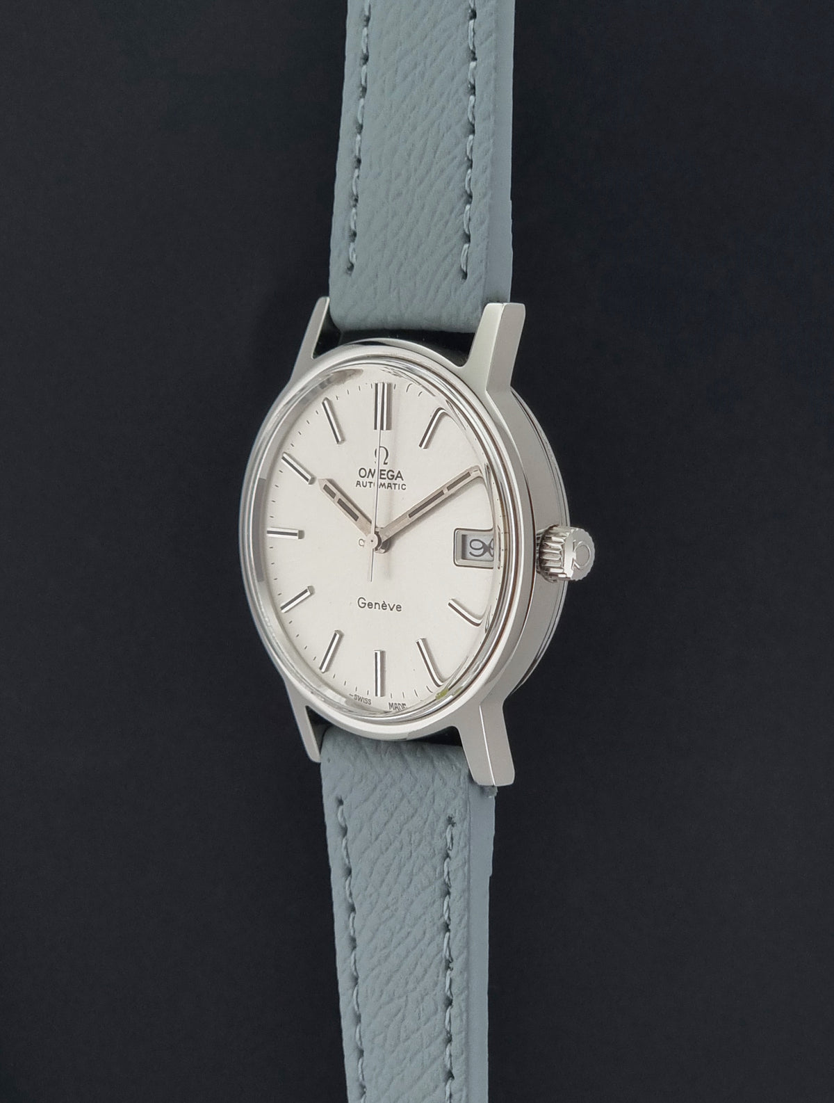 Vintage Omega Geneve 166.0163 Wristwatch with a silver-toned case, white dial, and a light grey leather strap, shown against a dark background.