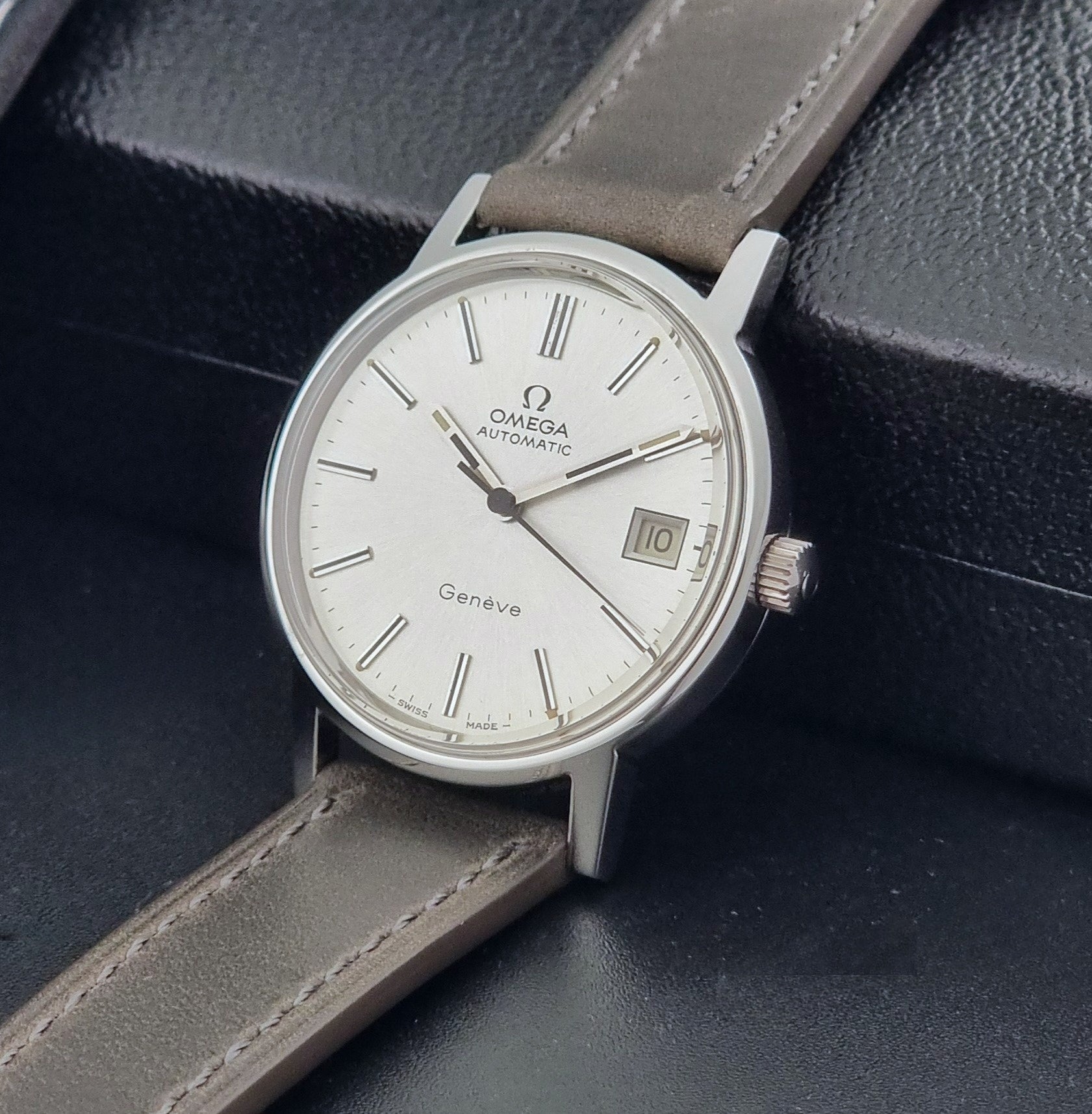 Vintage Omega Geneve 166.0163 watch with gray leather strap on a dark background crown view