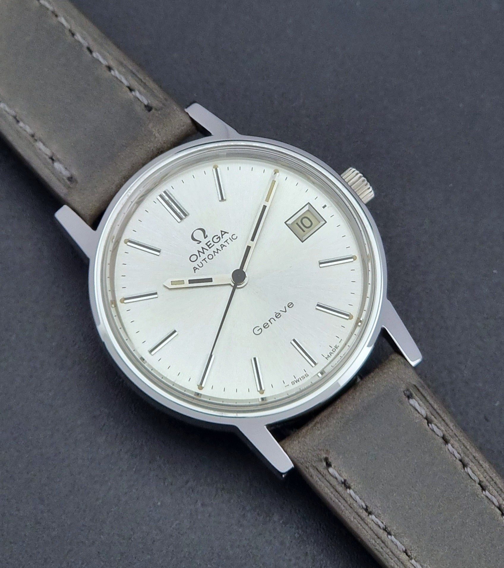 Vintage Omega Geneve 166.0163 watch with gray leather strap on a dark background close up dial view