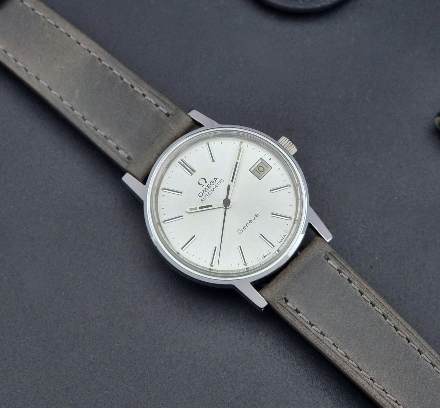 Vintage Omega Geneve 166.0163 watch with gray leather strap on a dark background dial