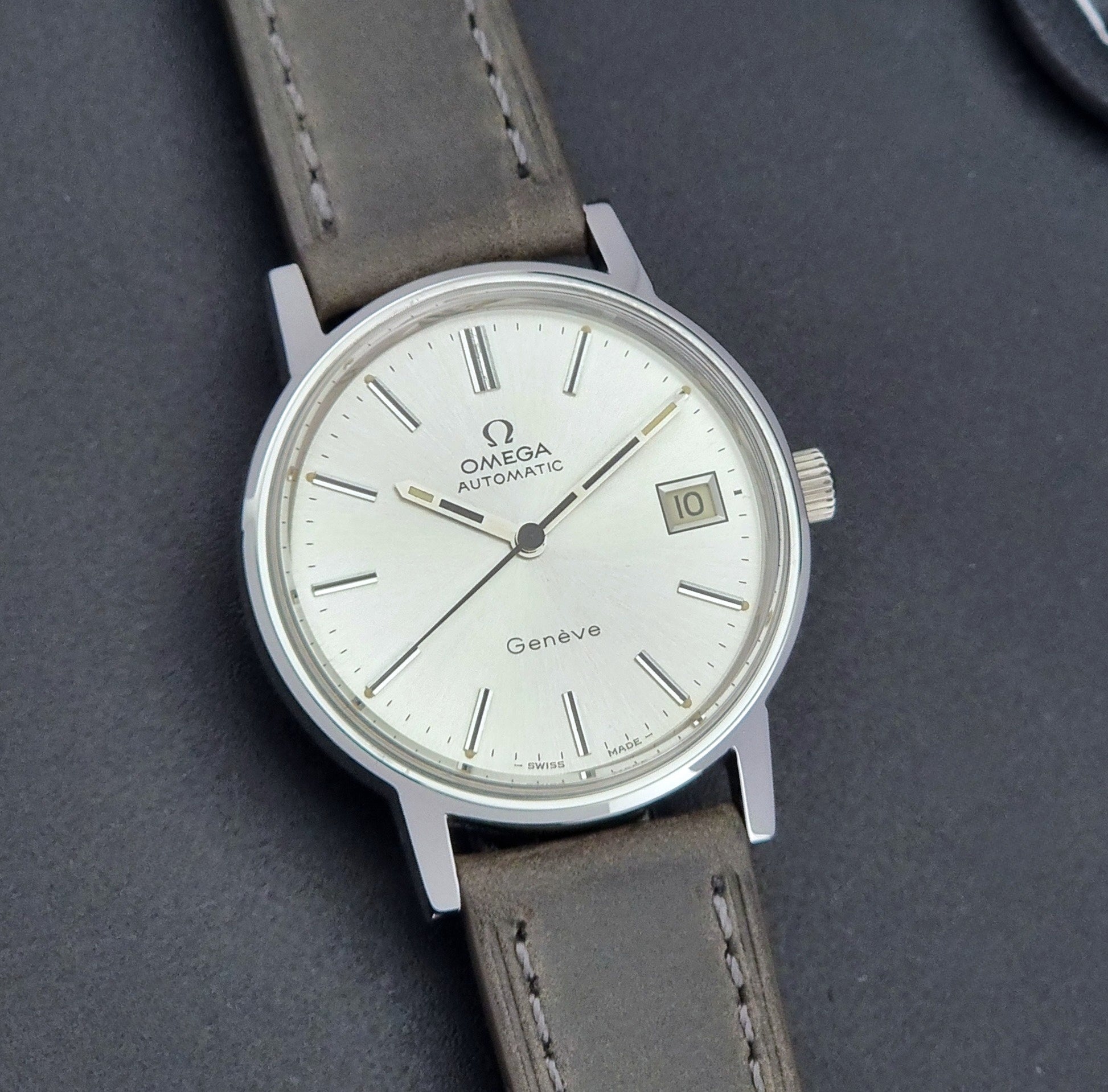 Vintage Omega Geneve 166.0163 watch with gray leather strap on a dark background front view