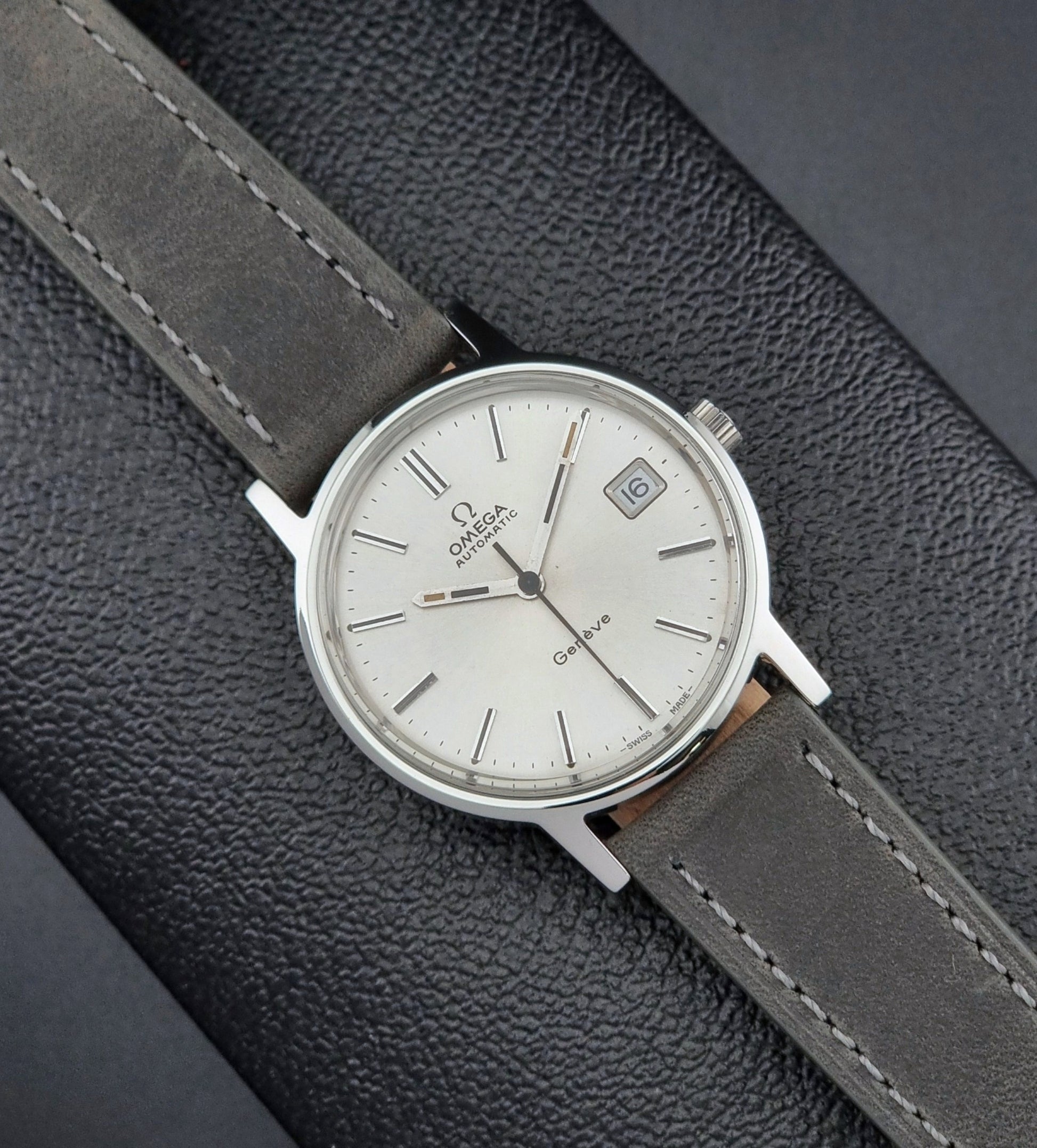 Vintage Omega watch with a silver case and gray leather strap on a textured gray background