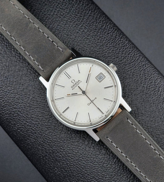 Vintage Omega watch with a silver case and gray leather strap on a textured gray background