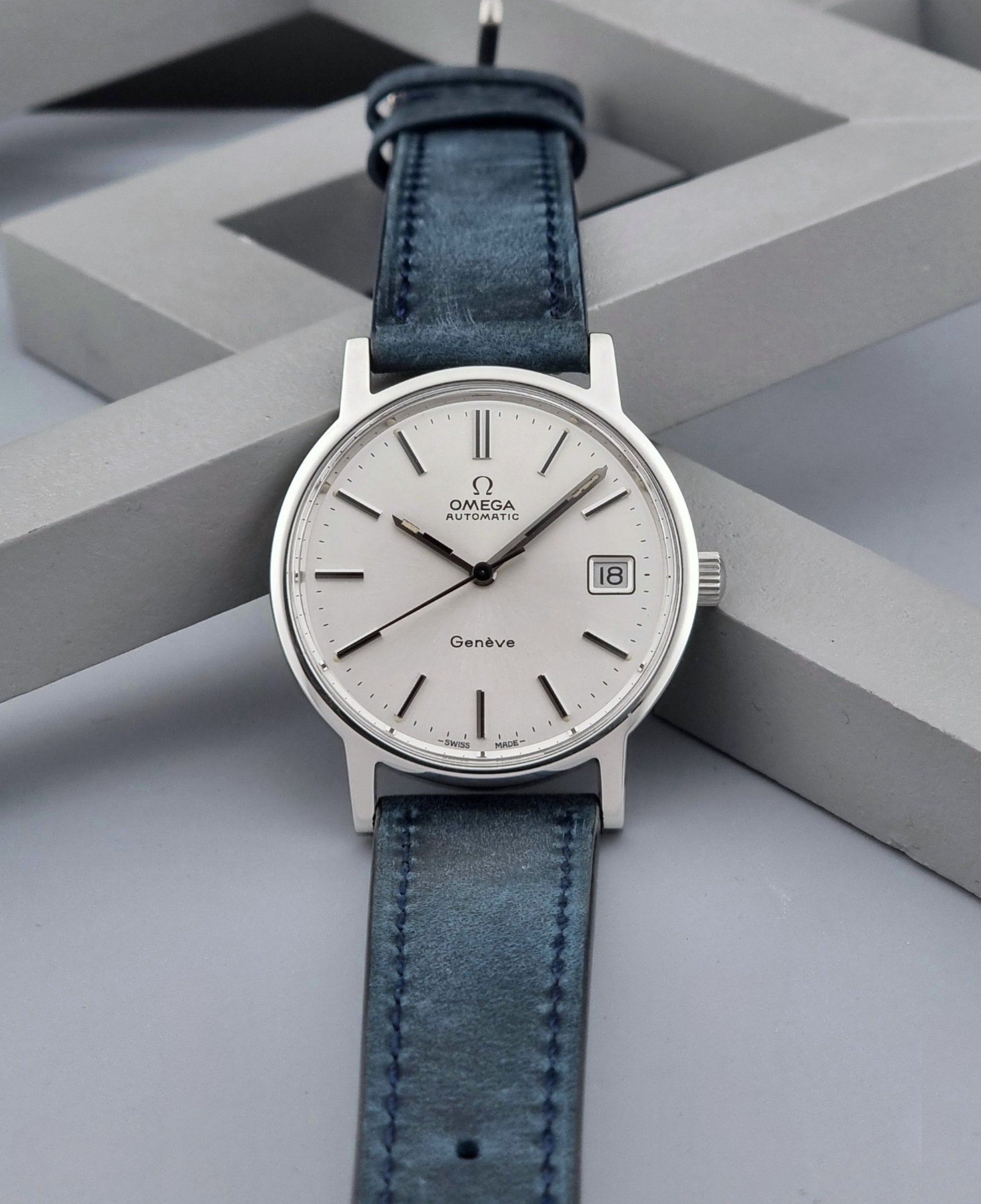 Vintage Omega Geneve 166.0163 wristwatch with blue leather strap on a geometric background