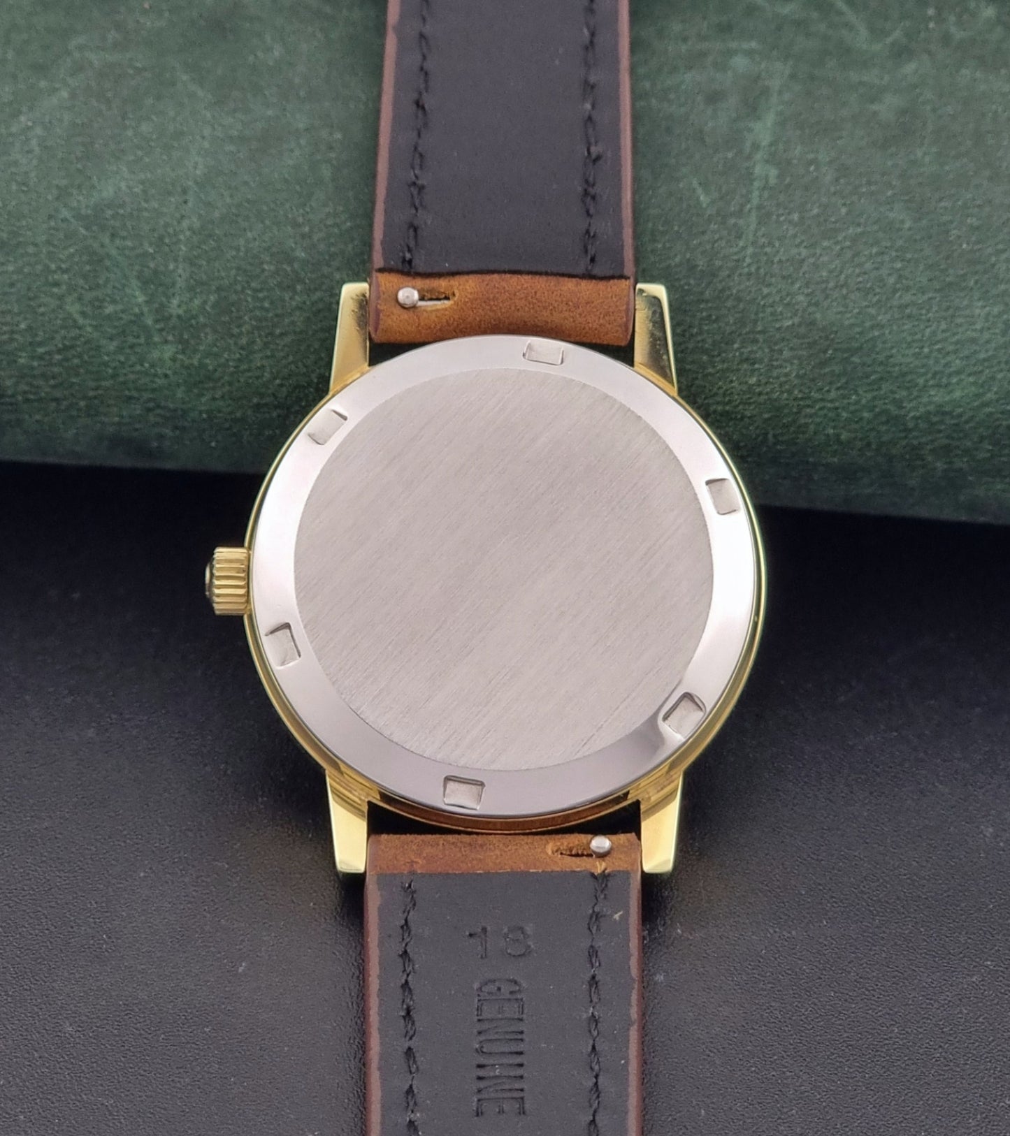 Vintage Omega Geneve Wristwatch 166.0163 in gold with brown leather strap on a dark gray background case back view