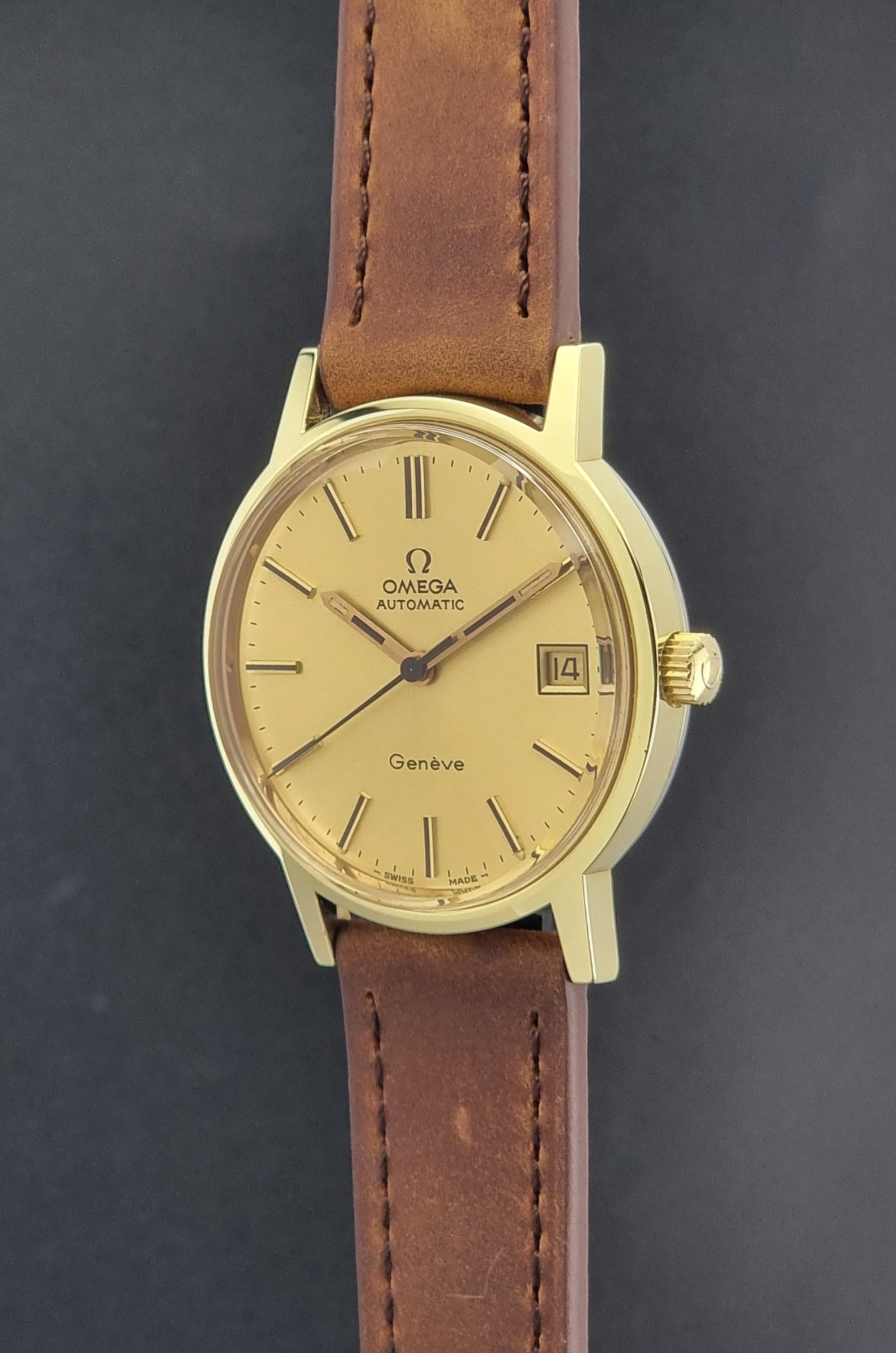 Vintage Omega Geneve Wristwatch 166.0163 in gold with brown leather strap on a dark gray background crown profile view