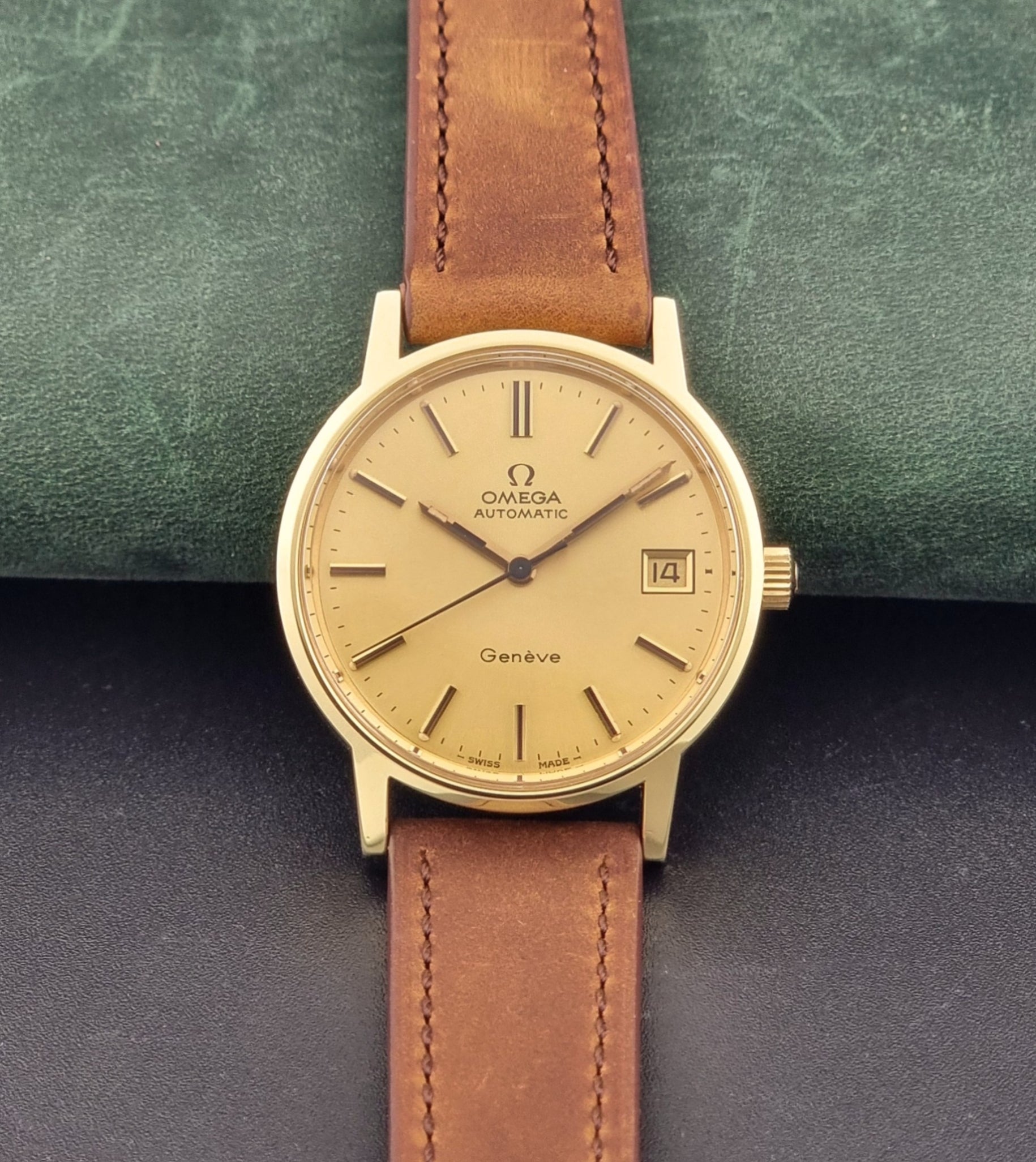 Vintage Omega Geneve Wristwatch 166.0163 in gold with brown leather strap on a dark gray background dial view