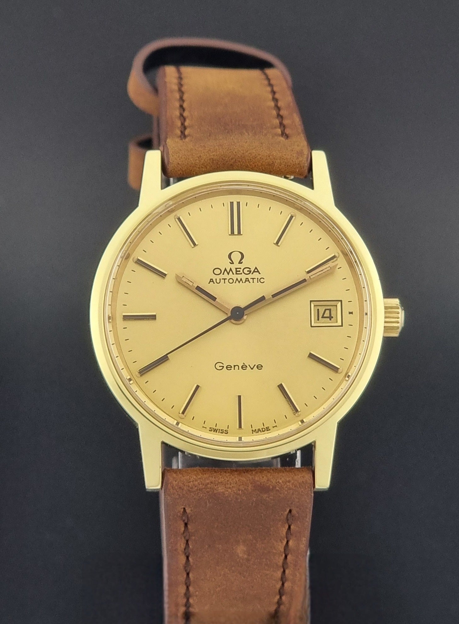 Vintage Omega Geneve Wristwatch 166.0163 in gold with brown leather strap on a dark gray background close dial view