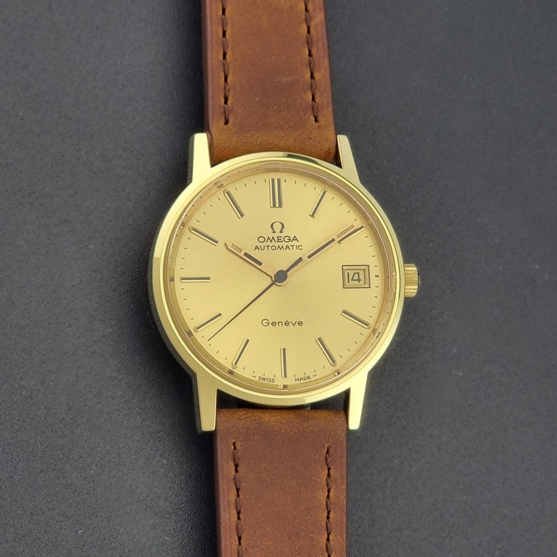 Vintage Omega Geneve Wristwatch 166.0163 in gold with brown leather strap on a dark gray background front view