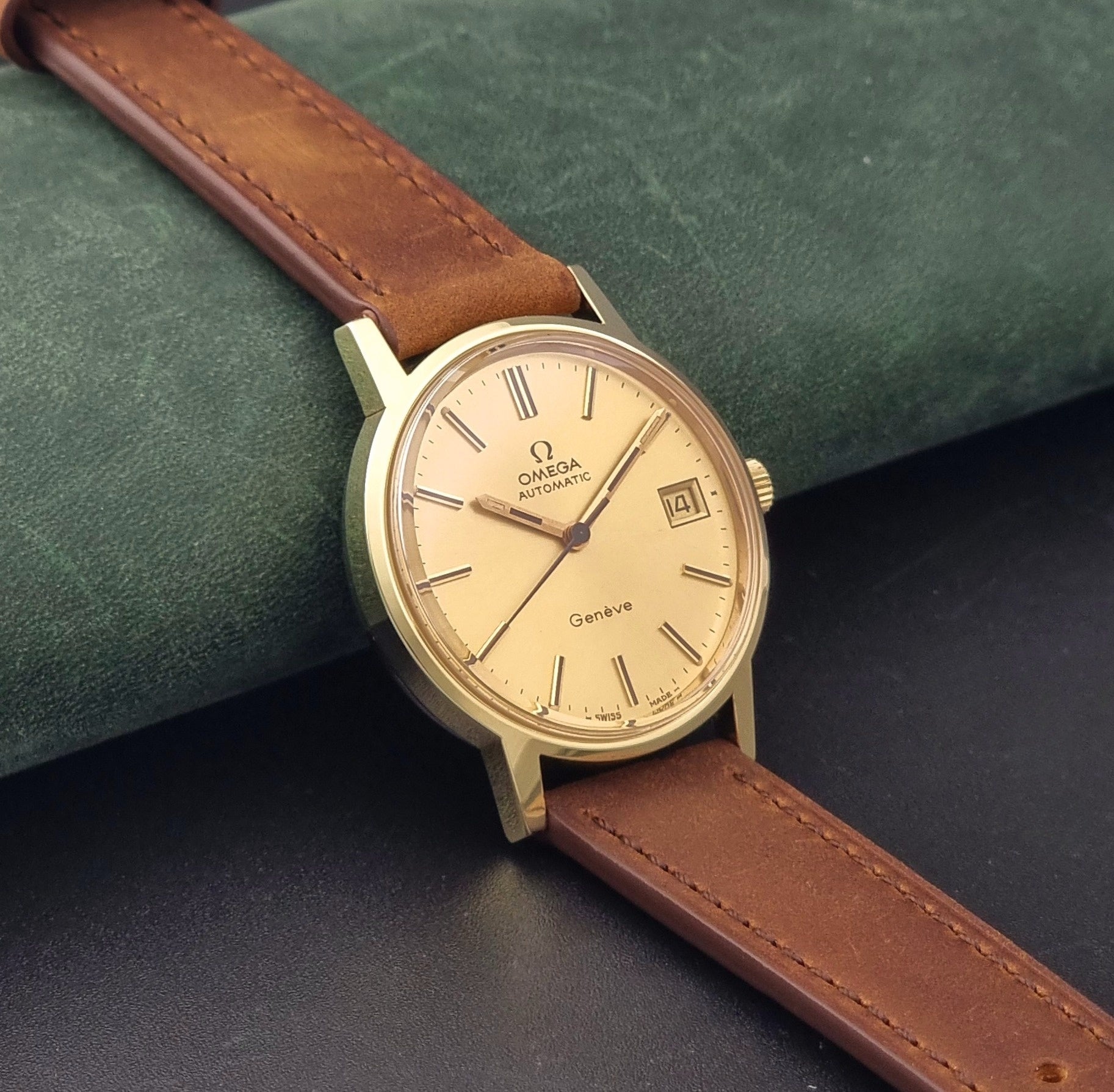 Vintage Omega Geneve Wristwatch 166.0163 in gold with brown leather strap on a dark gray background side view