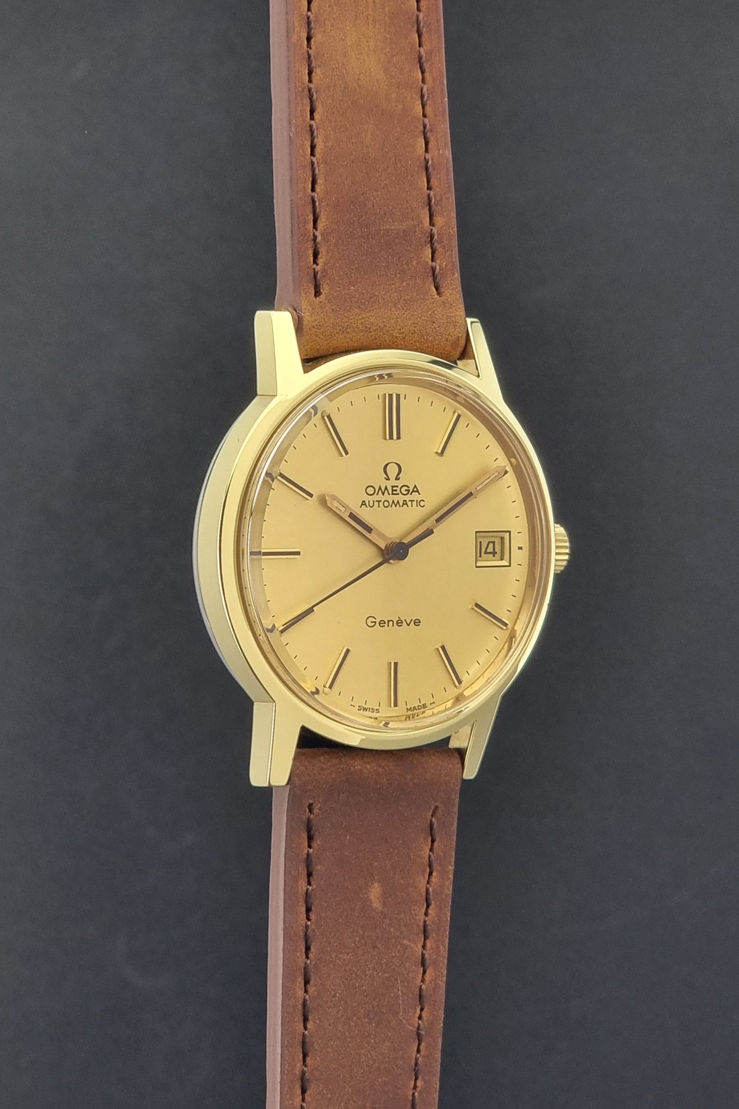 Vintage Omega Geneve Wristwatch 166.0163 in gold with brown leather strap on a dark gray background side profile view