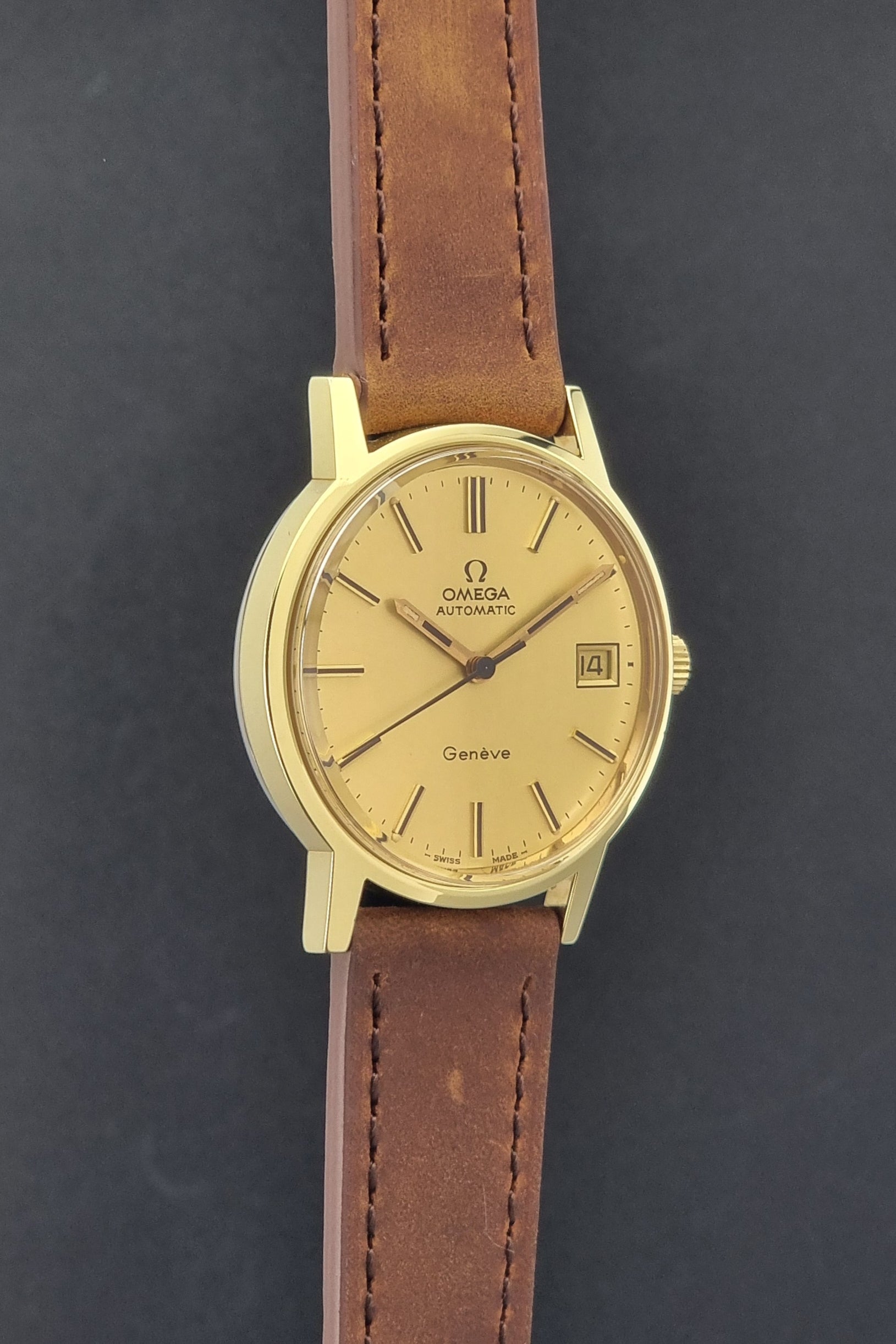 Vintage Omega Geneve Wristwatch 166.0163 in gold with brown leather strap on a dark gray background side profile view