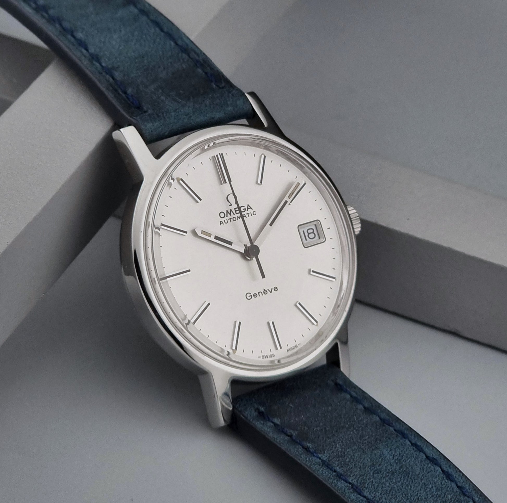Vintage Omega Geneve 166.0163 wristwatch with blue strap on a gray surface