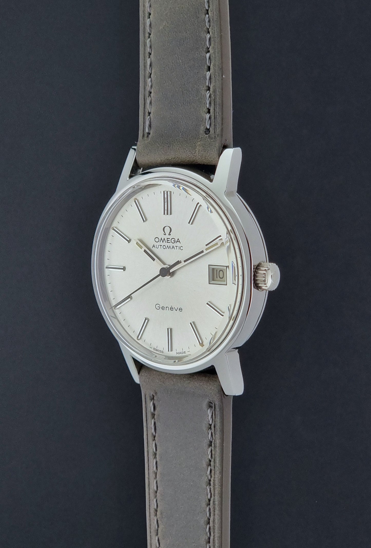 Vintage Omega Geneve 166.0163 watch with gray leather strap on a dark background crown view