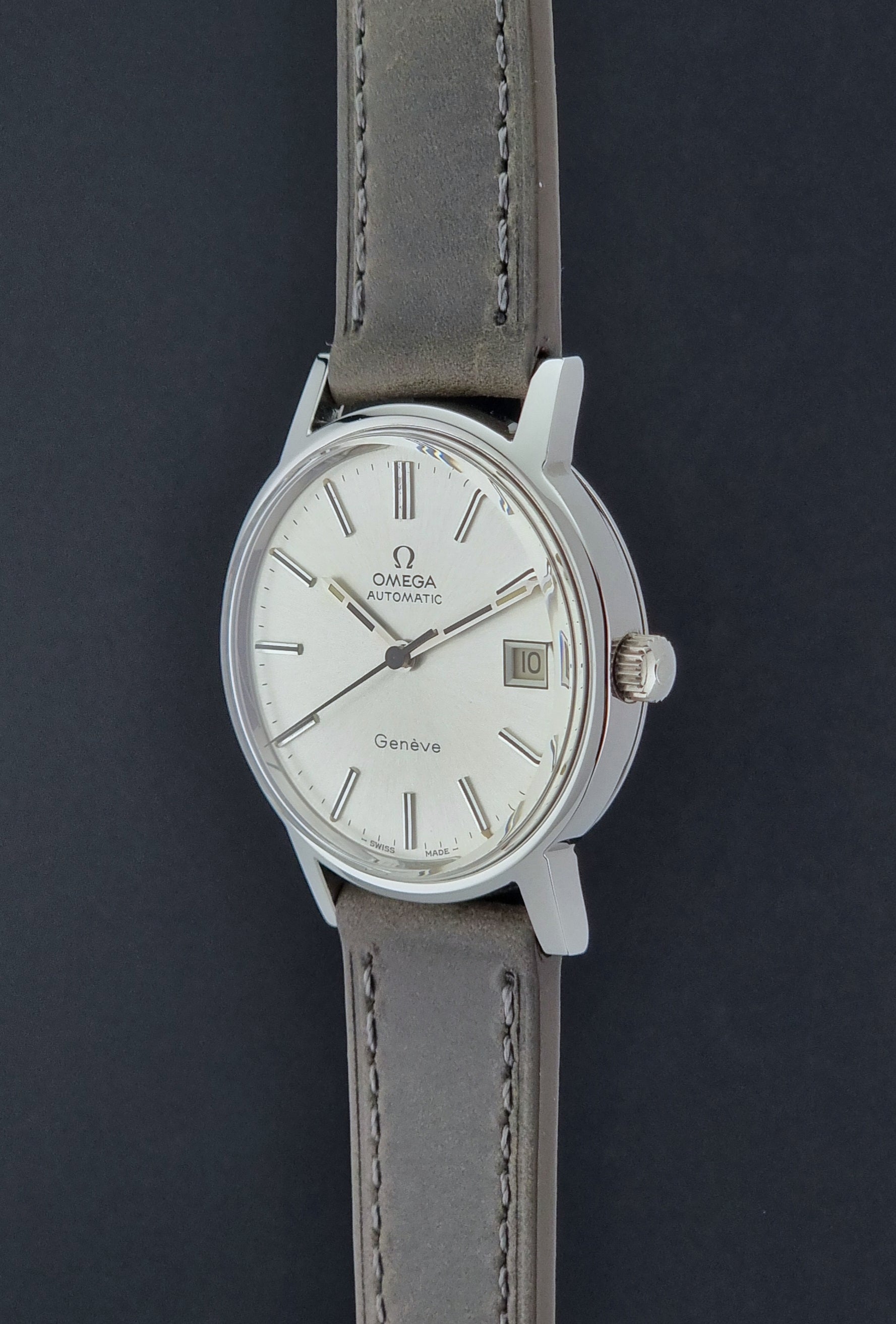 Vintage Omega Geneve 166.0163 watch with gray leather strap on a dark background crown view