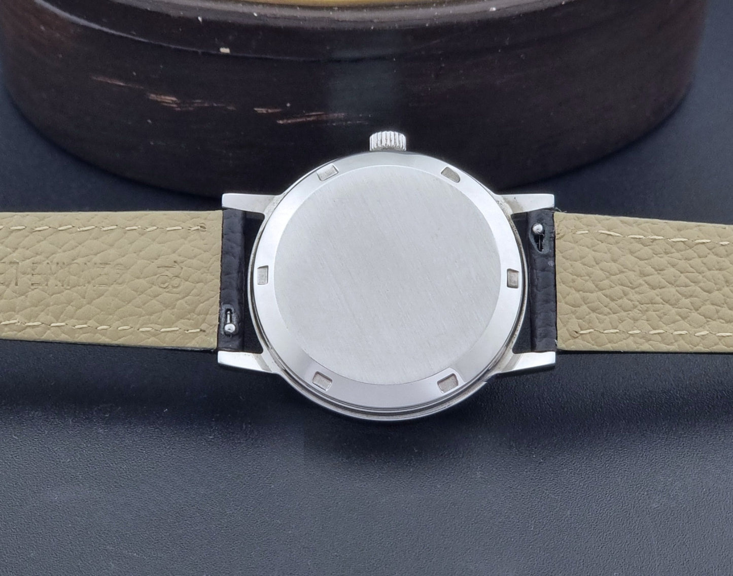 Vintage Omega Geneve Wristwatch 166.0163 with black leather strap and silver case on a dark gray background case back view