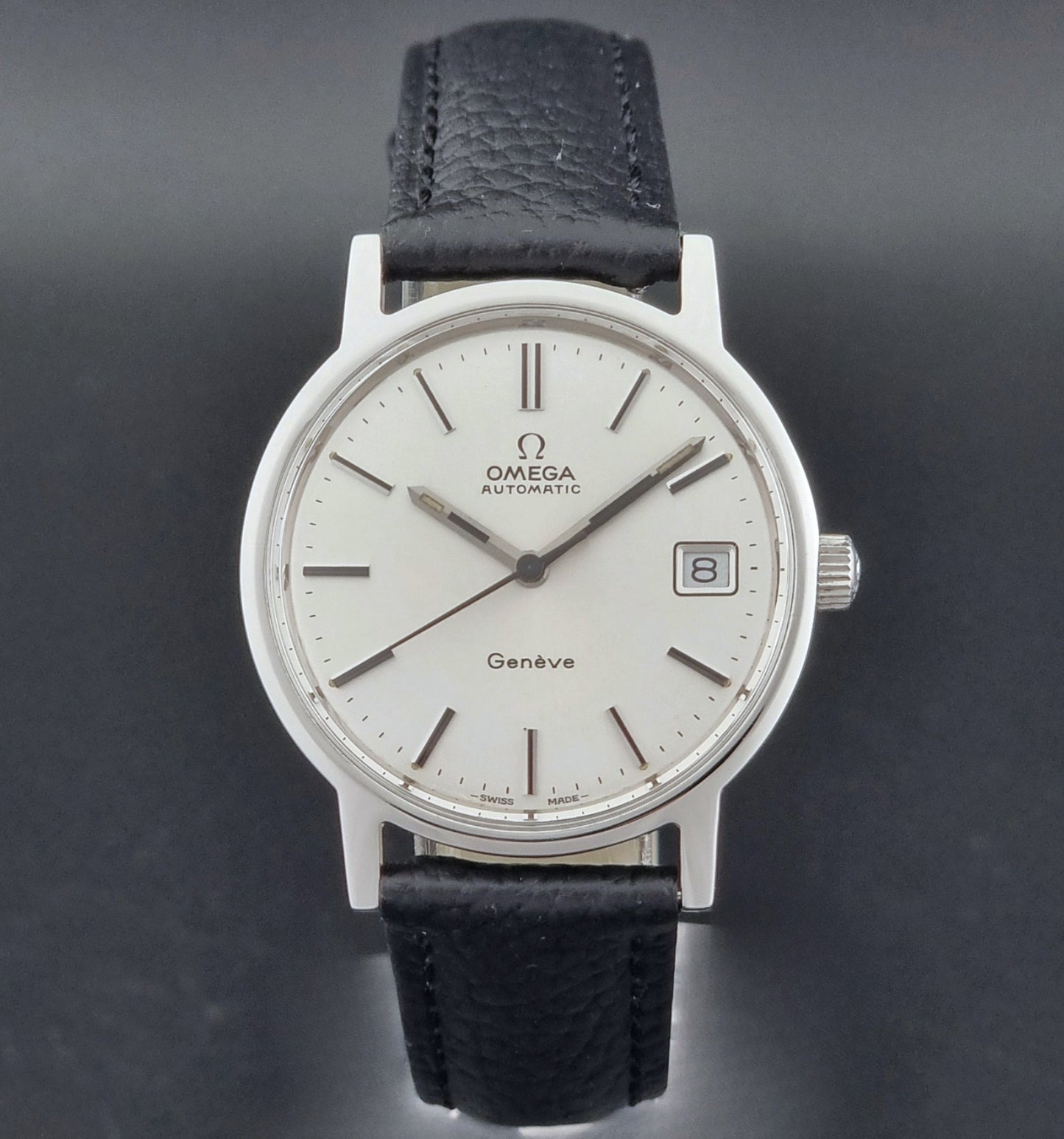 Vintage Omega Geneve Wristwatch 166.0163 with black leather strap and silver case on a dark gray background close dial view