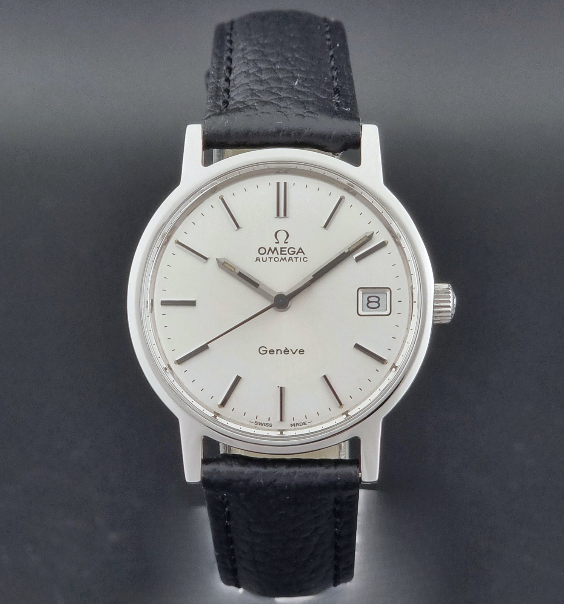 Vintage Omega Geneve Wristwatch 166.0163 with black leather strap and silver case on a dark gray background close dial view