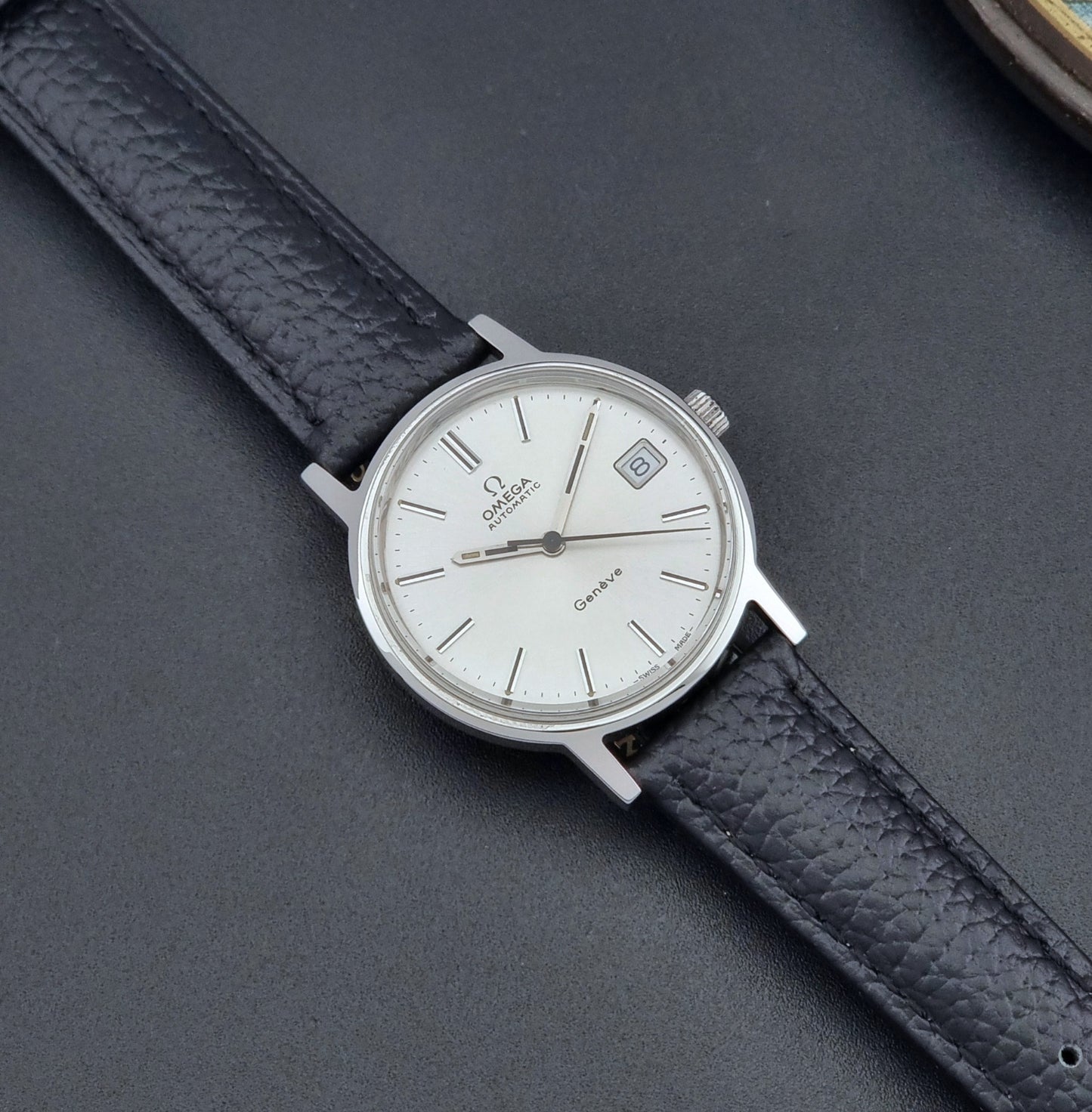 Vintage Omega Geneve Wristwatch 166.0163 with black leather strap and silver case on a dark gray background dial