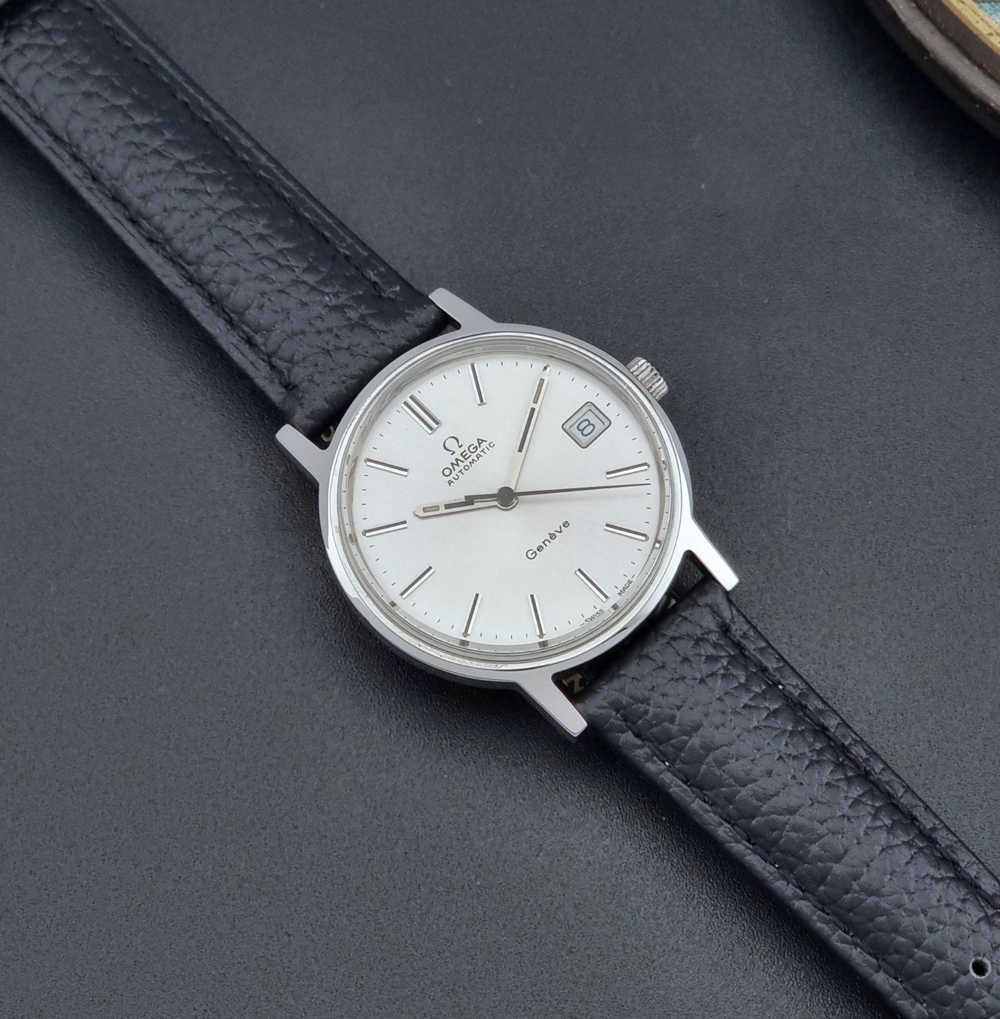 Vintage Omega Geneve Wristwatch 166.0163 with black leather strap and silver case on a dark gray background dial