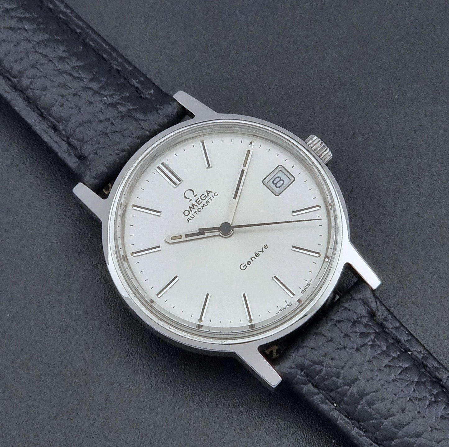Vintage Omega Geneve Wristwatch 166.0163 with black leather strap and silver case on a dark gray background close up dial view