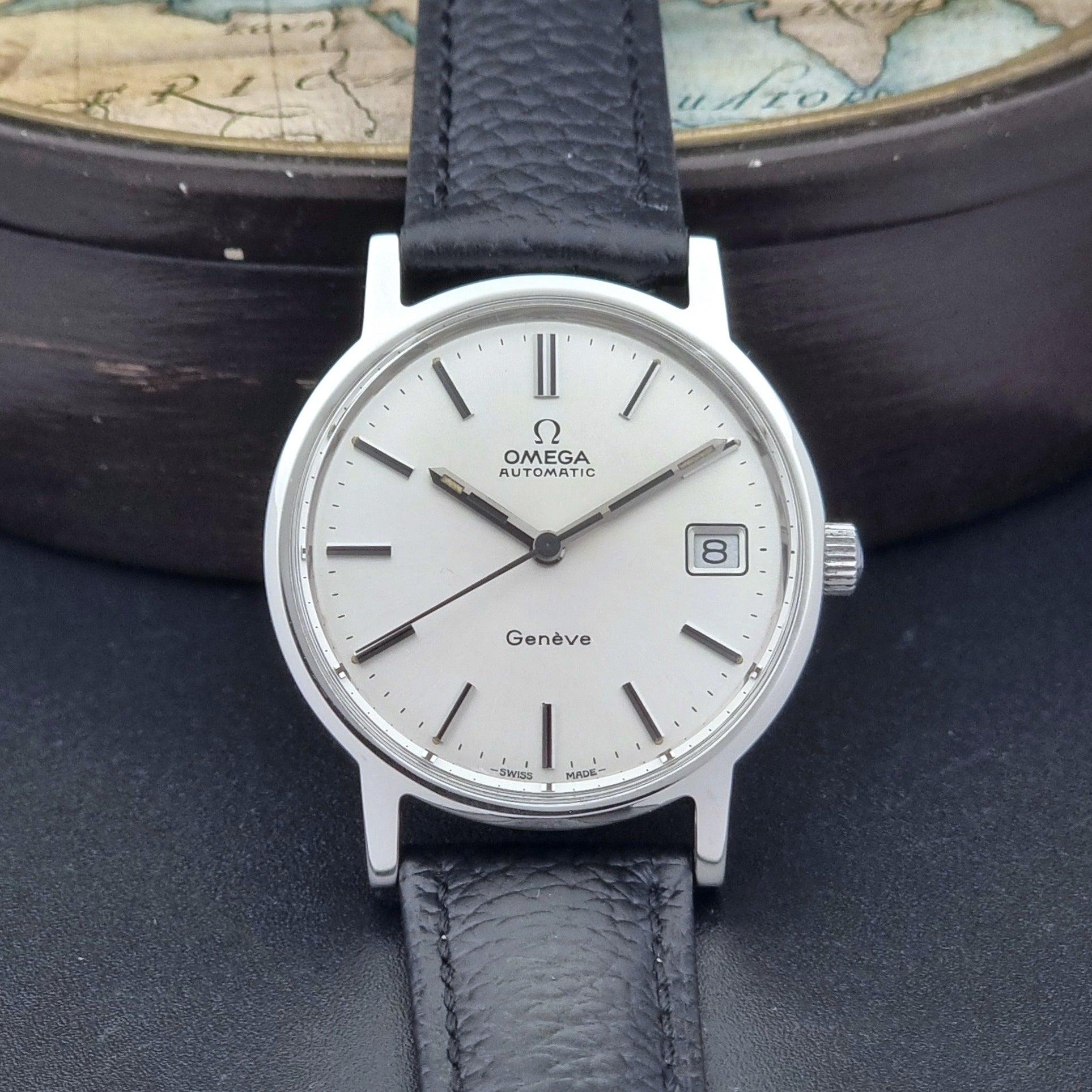 Vintage Omega Geneve Wristwatch 166.0163 with black leather strap and silver case on a dark gray background dial view