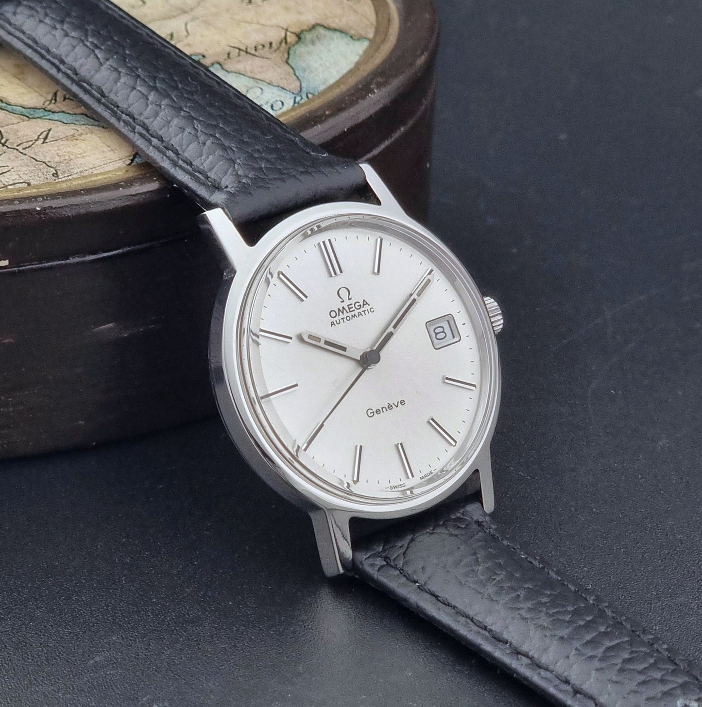 Vintage Omega Geneve Wristwatch 166.0163 with black leather strap and silver case on a dark gray background side view