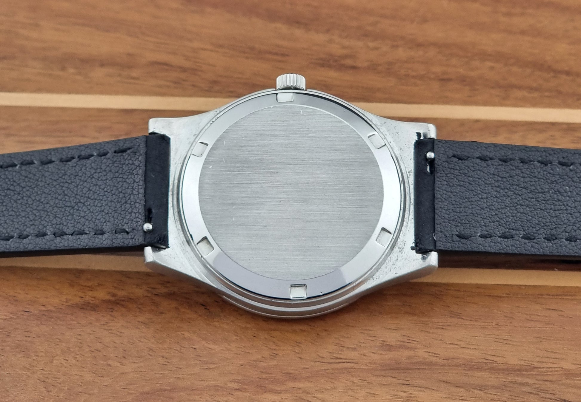 Vintage Omega Geneve 166.0169 wristwatch with a black strap on a wooden surface case back view