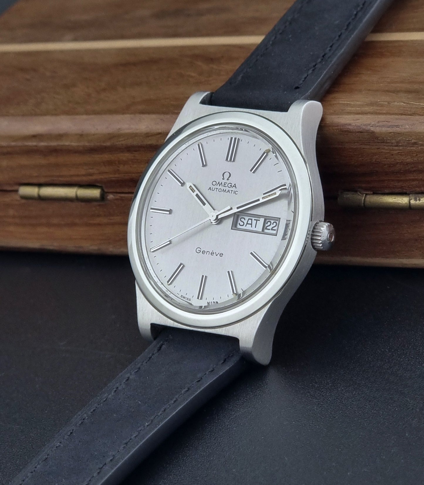 Vintage Omega Geneve 166.0169 wristwatch with a black strap on a wooden surface crown view