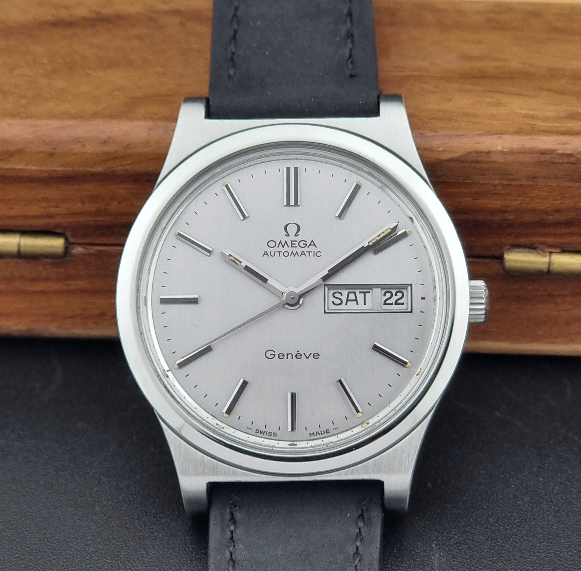 Vintage Omega Geneve 166.0169 wristwatch with a black strap on a wooden surface close up dial view