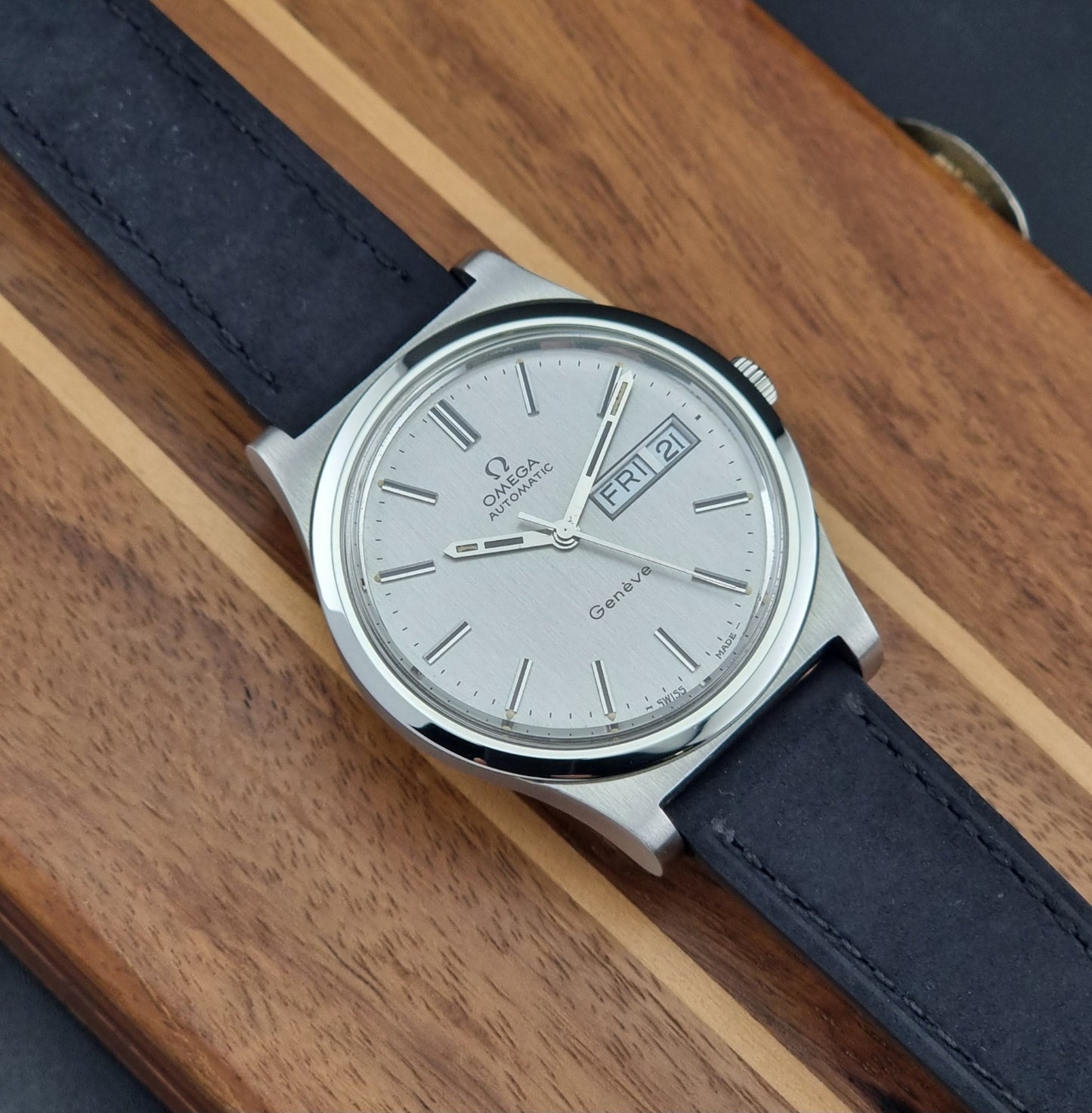 Vintage Omega Geneve 166.0169 wristwatch with a black strap on a wooden surface front