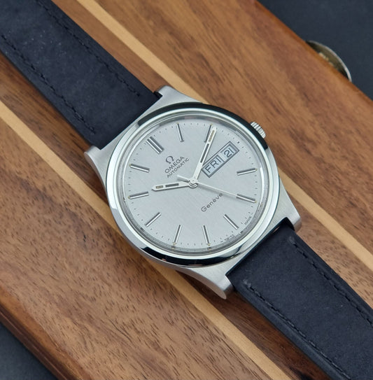 Vintage Omega Geneve 166.0169 wristwatch with a black strap on a wooden surface front