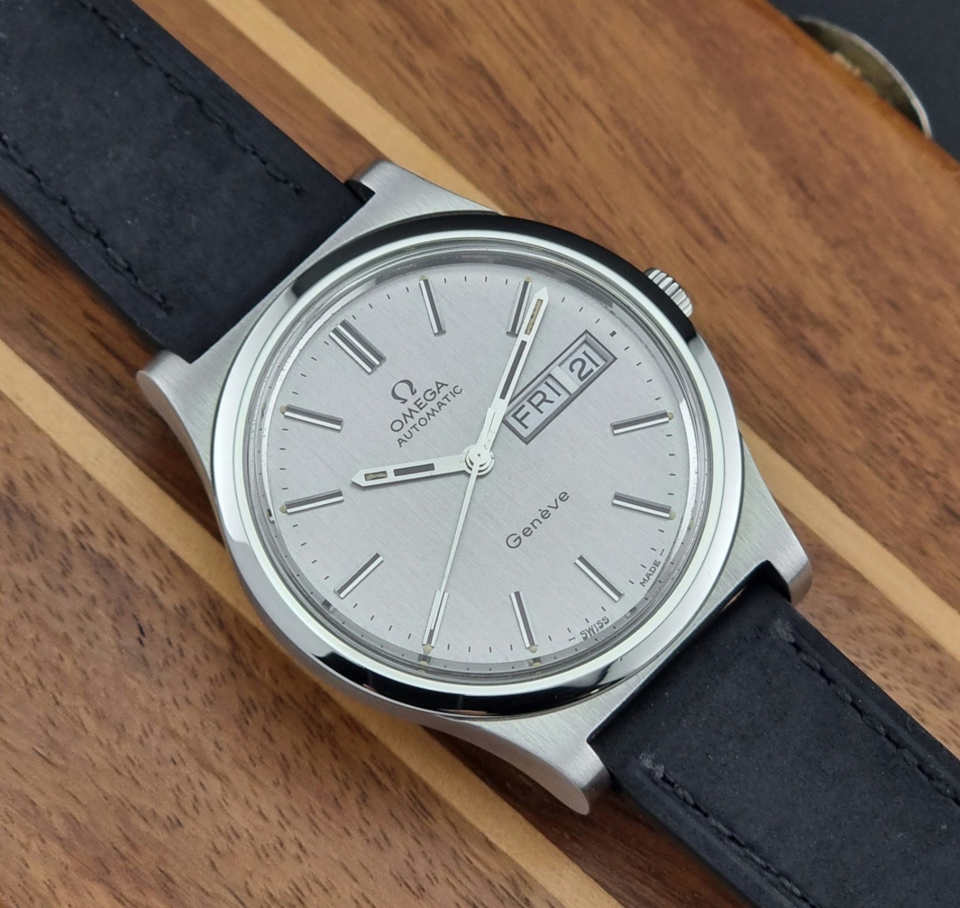 Vintage Omega Geneve 166.0169 wristwatch with a black strap on a wooden surface dial view