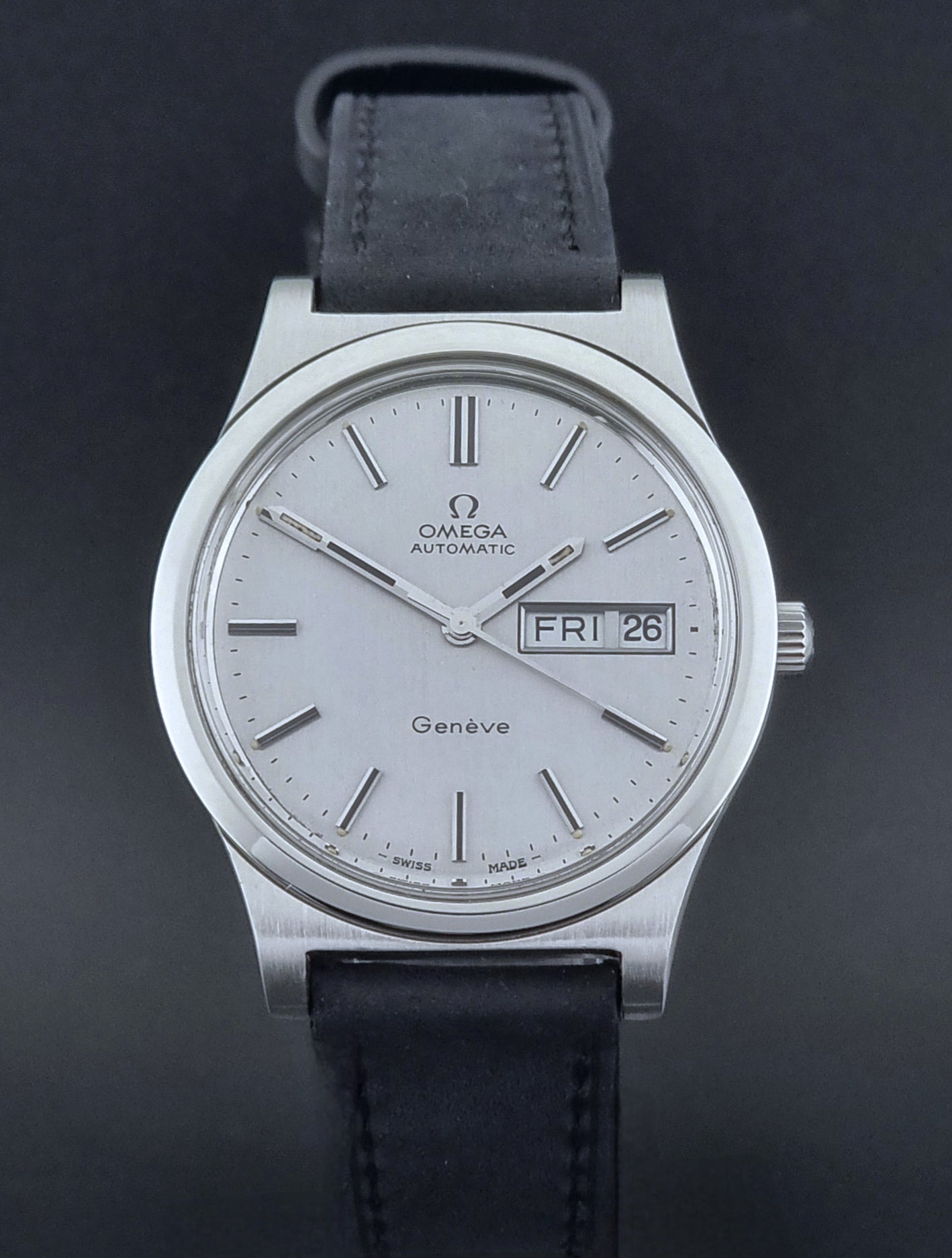 Vintage Omega Geneve 166.0169 wristwatch with a black strap on a dark background close front view