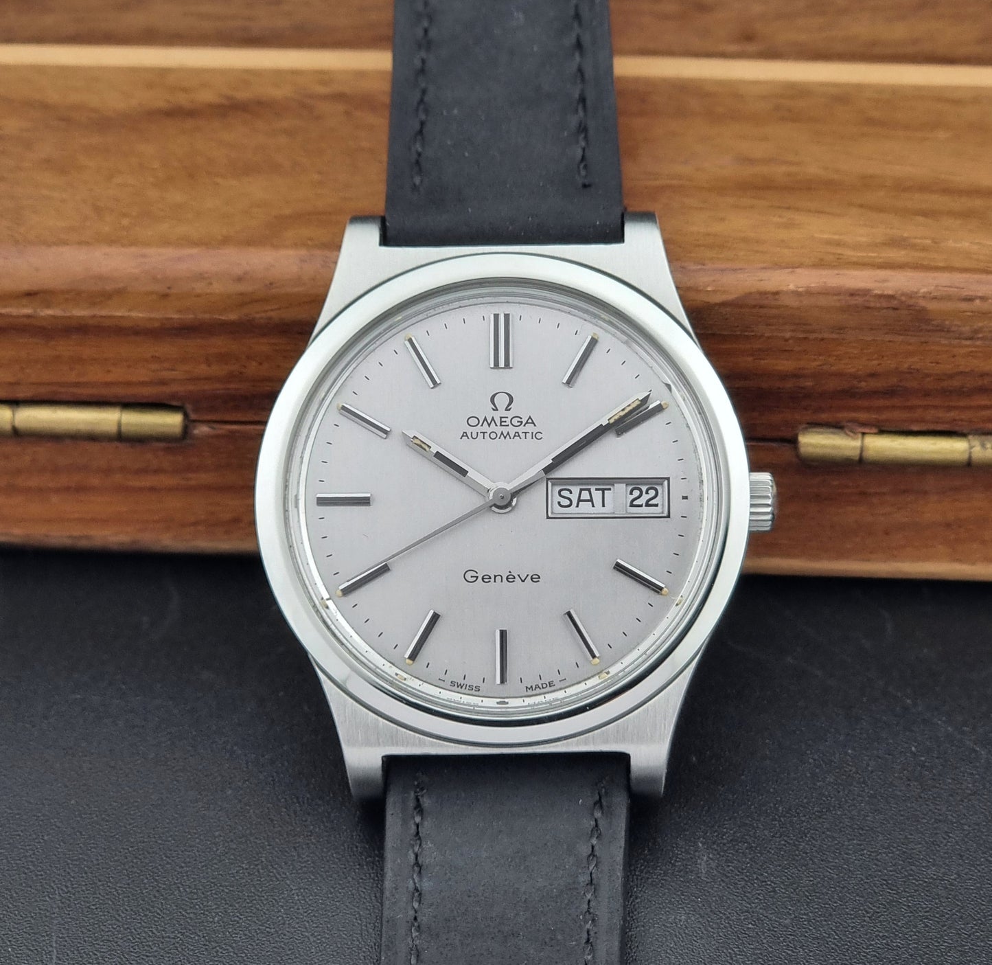 Vintage Omega Geneve 166.0169 wristwatch with a black strap on a wooden surface front view