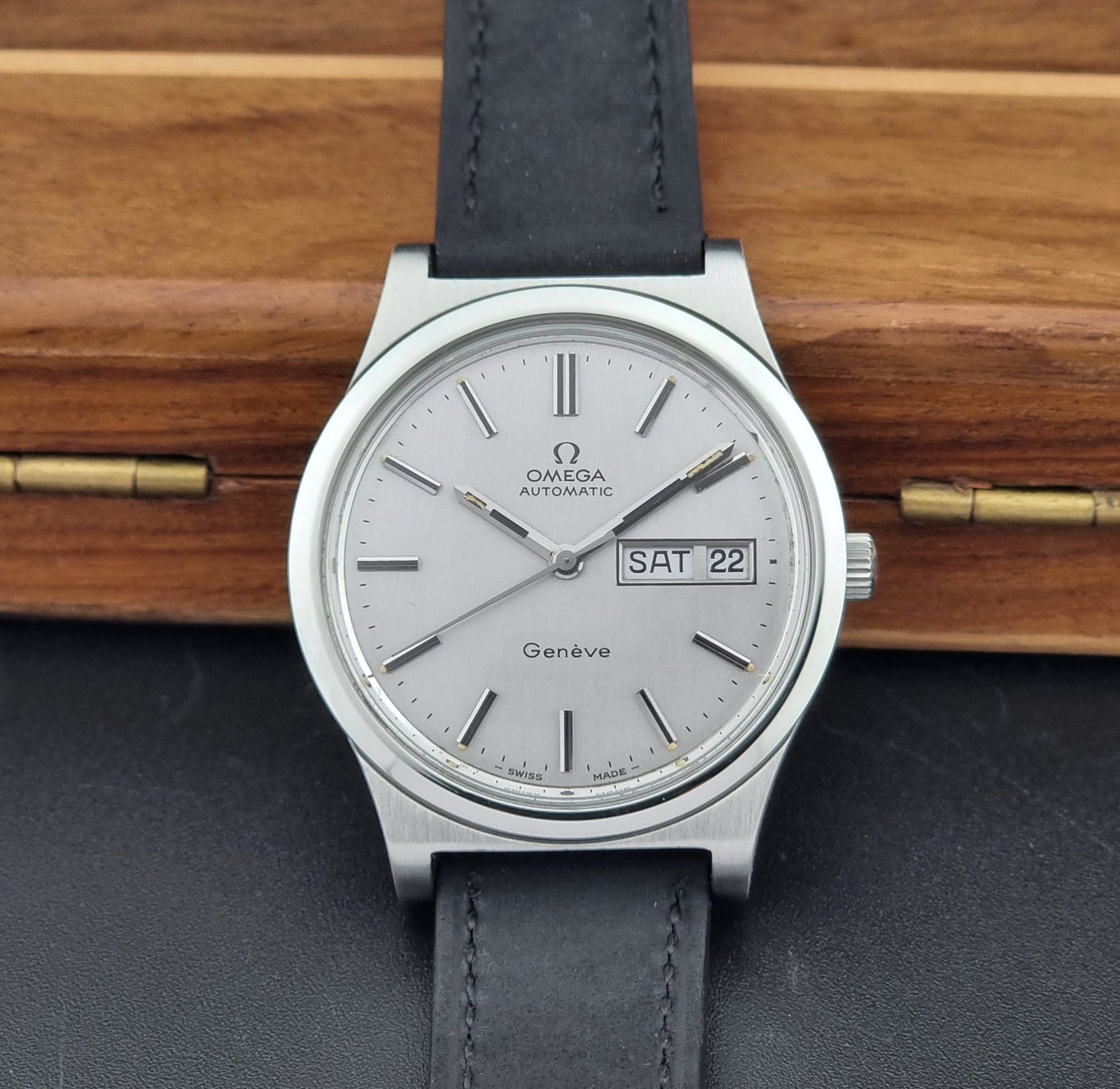 Vintage Omega Geneve 166.0169 wristwatch with a black strap on a wooden surface front view