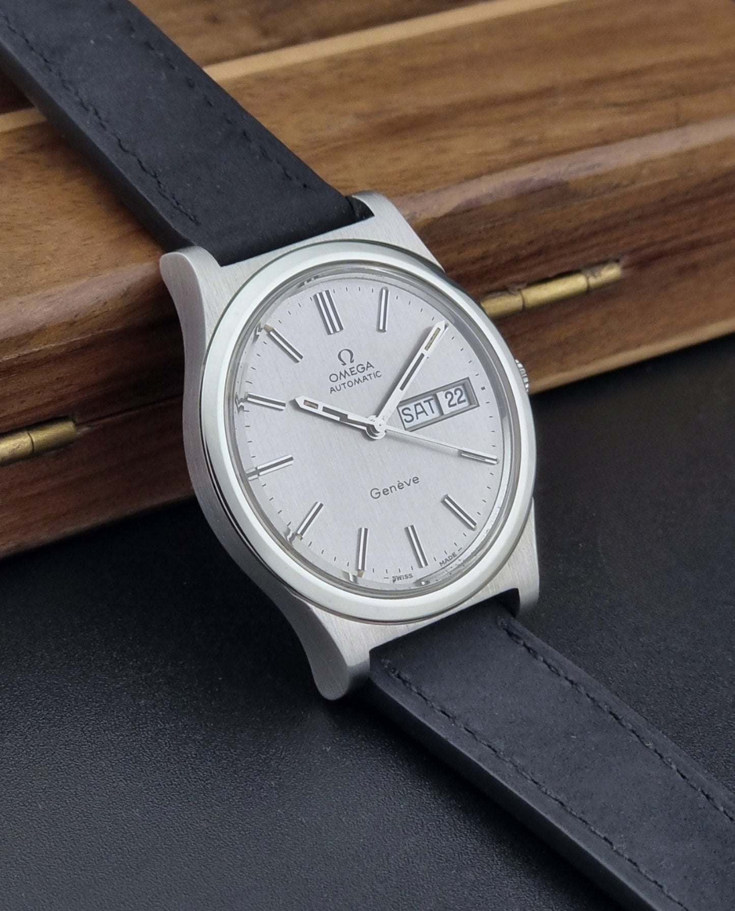 Vintage Omega Geneve 166.0169 wristwatch with a black strap on a wooden surface side view