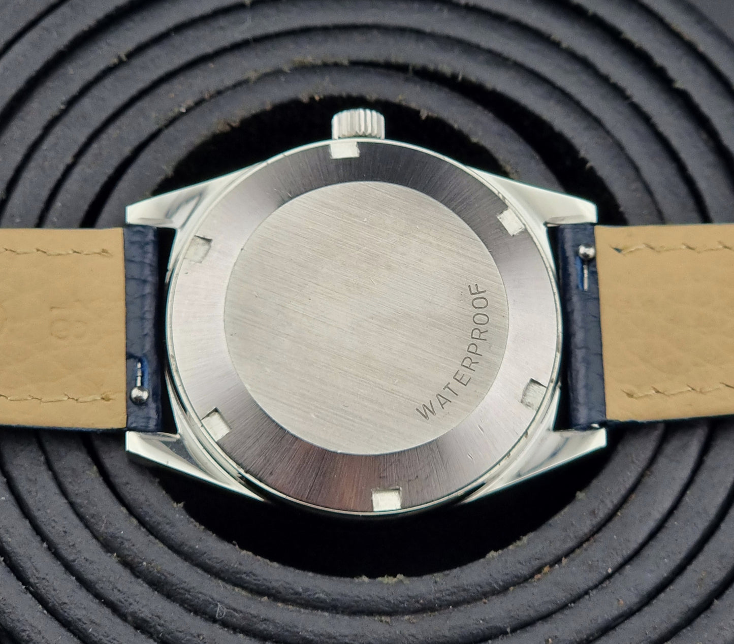 Close-up of a Vintage Omega Geneve watch case back on a textured black background