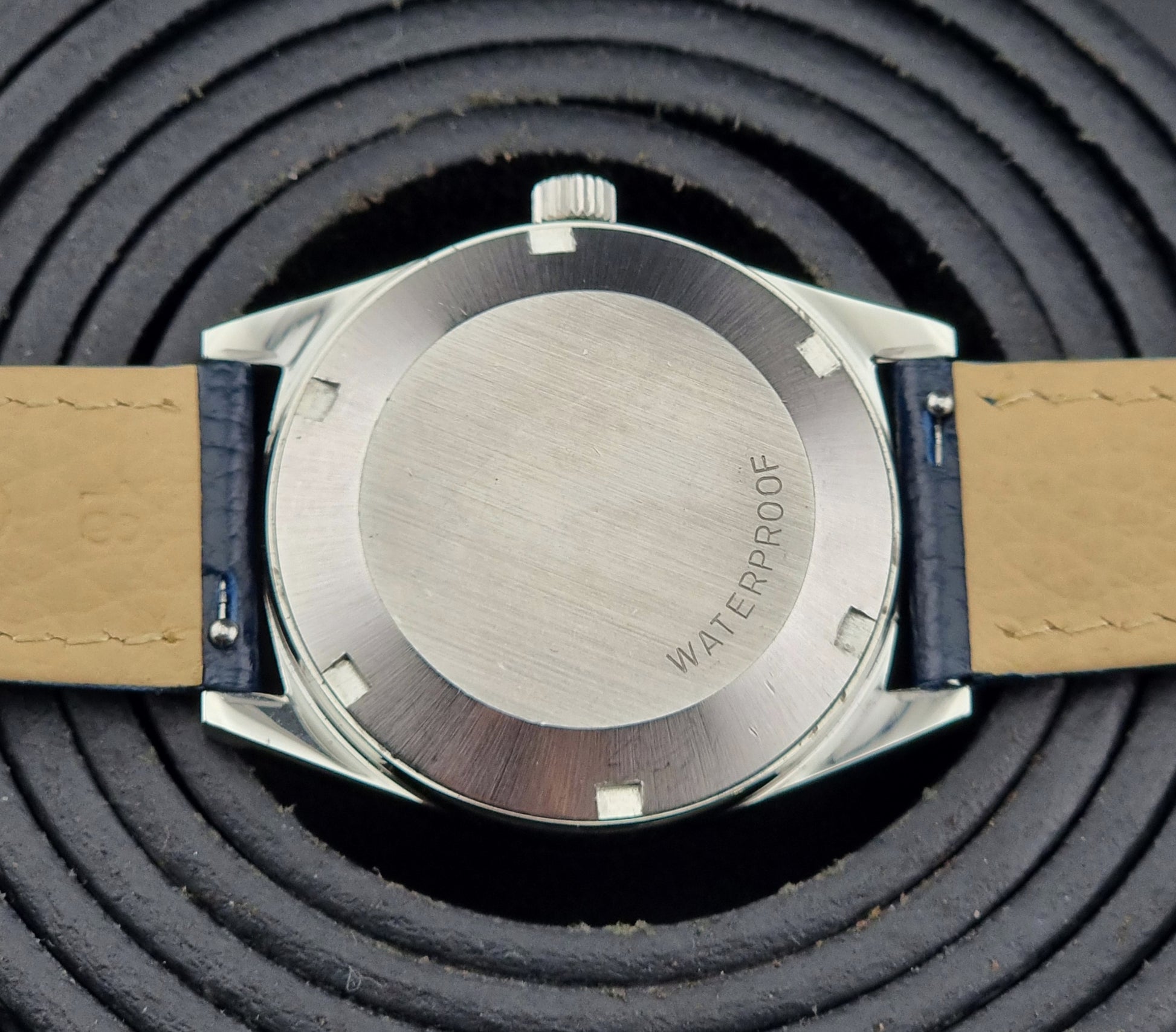 Close-up of a Vintage Omega Geneve watch case back on a textured black background