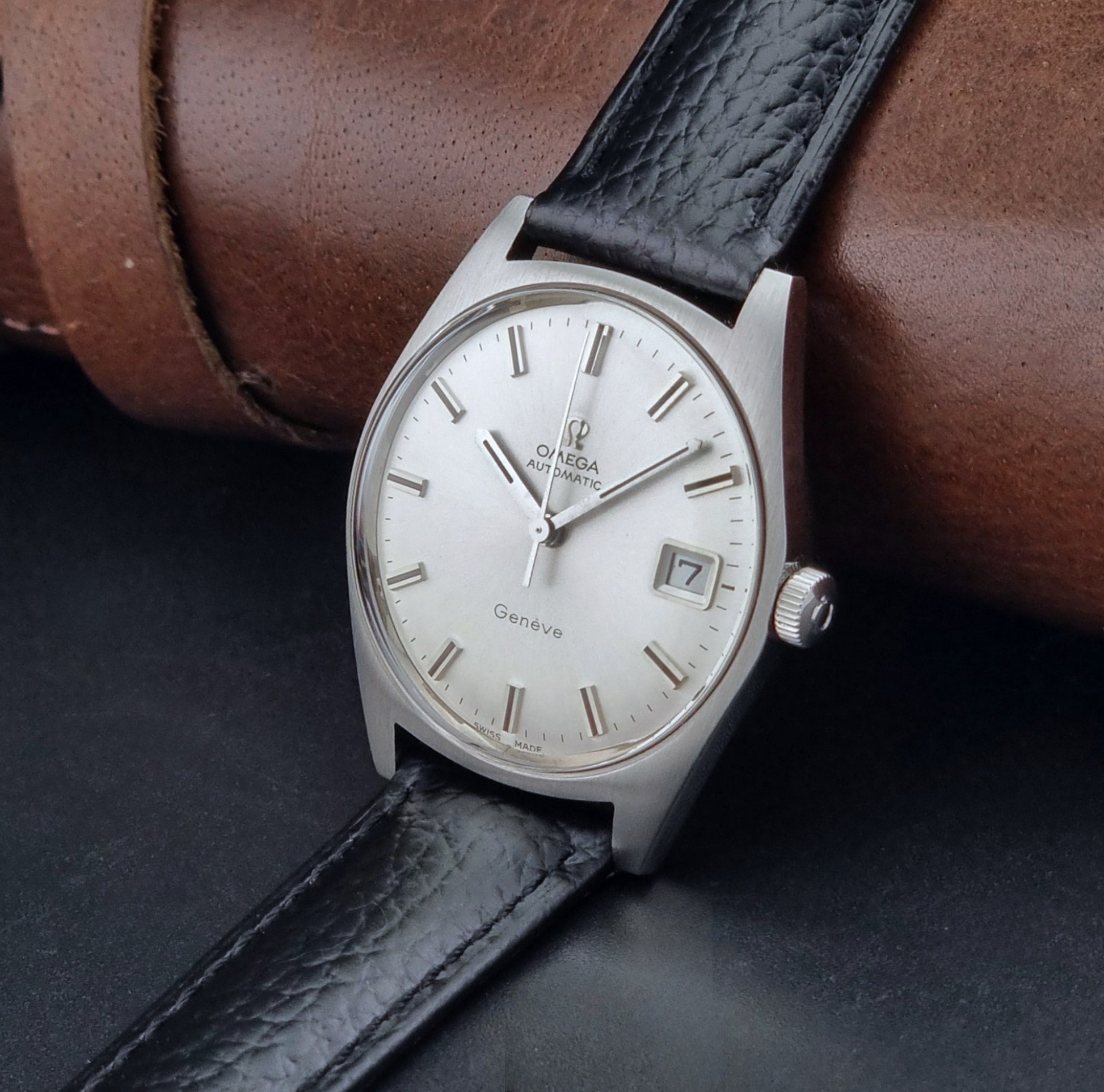 Vintage Omega Wristwatch a Geneve 166.041 with black leather strap on a dark surface crown view