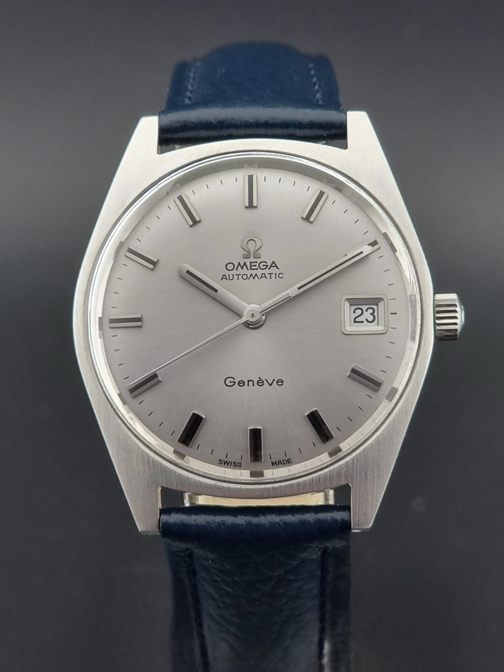Vintage Omega Geneve watch with silver dial and blue leather strap on a dark background
