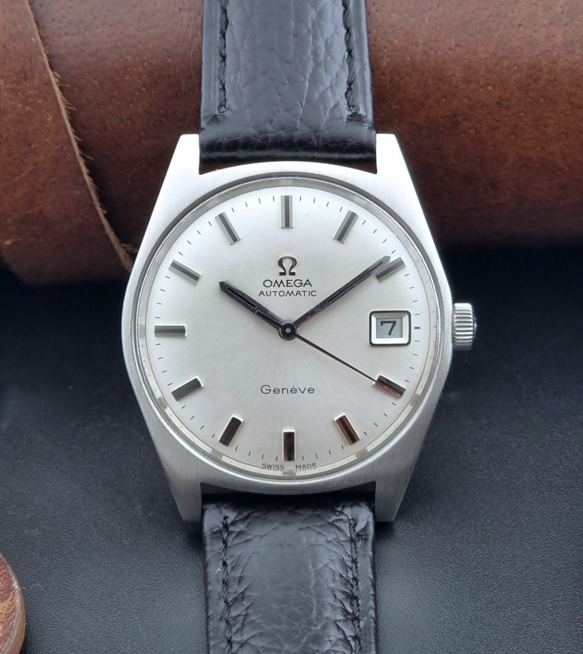 Vintage Omega Wristwatch a Geneve 166.041 with black leather strap on a dark surface front dial view