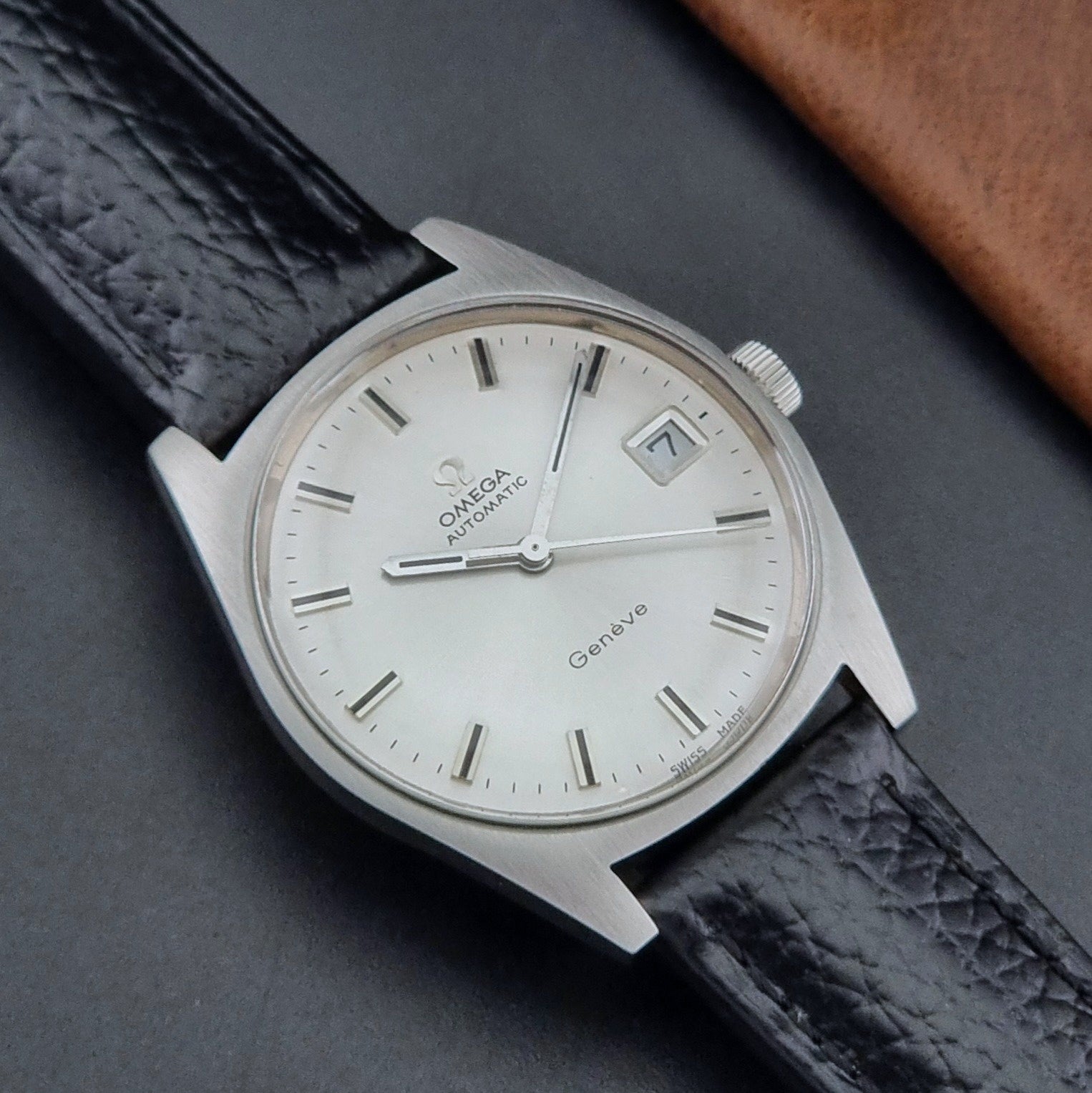 Vintage Omega Wristwatch a Geneve 166.041 with black leather strap on a dark surface close up dial view