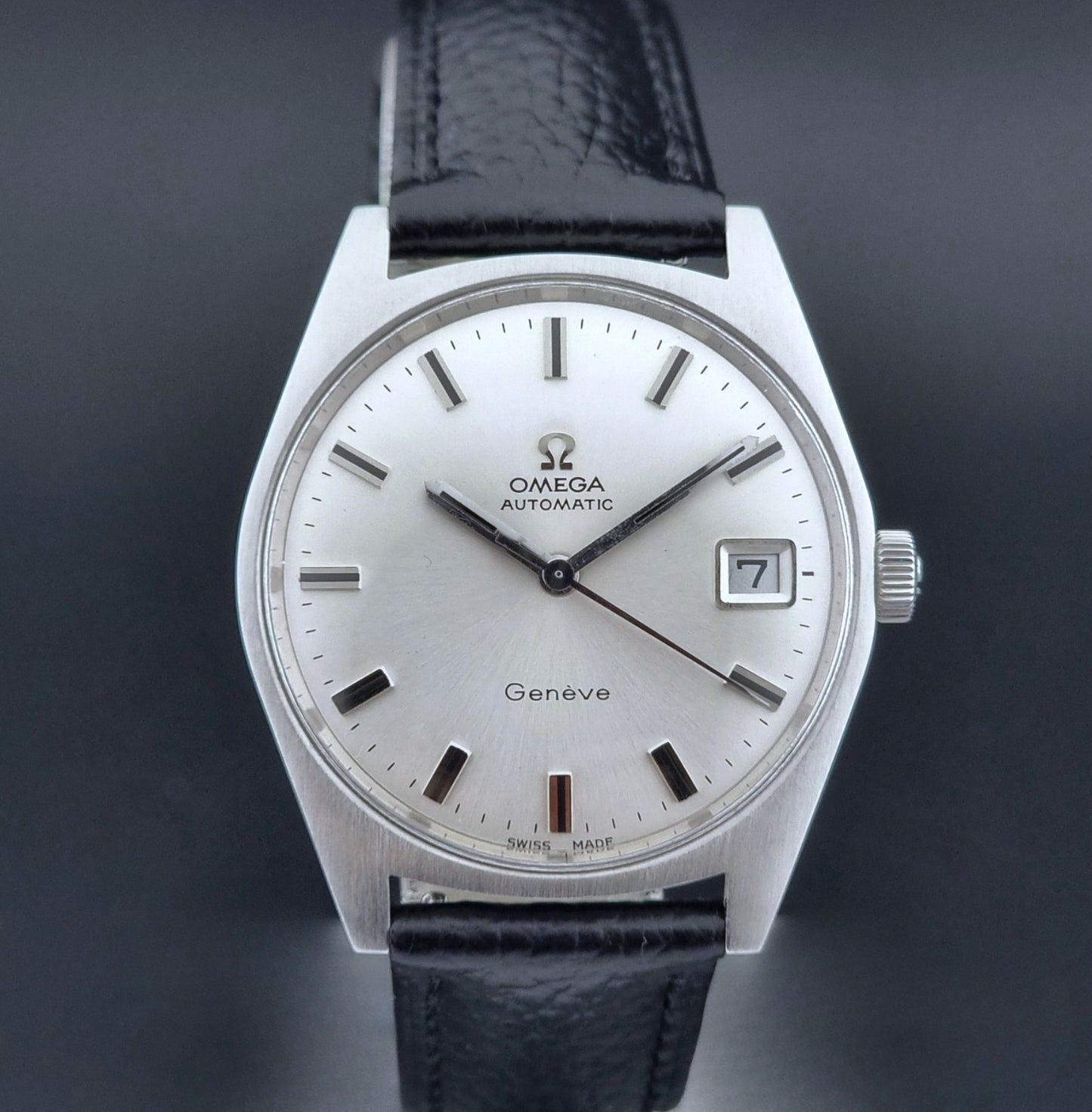 Vintage Omega Wristwatch a Geneve 166.041 with black leather strap on a dark surface close dial view