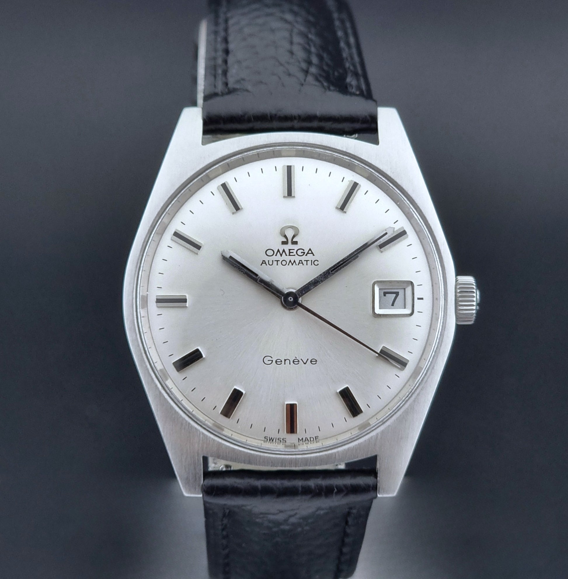 Vintage Omega Wristwatch a Geneve 166.041 with black leather strap on a dark surface close dial view