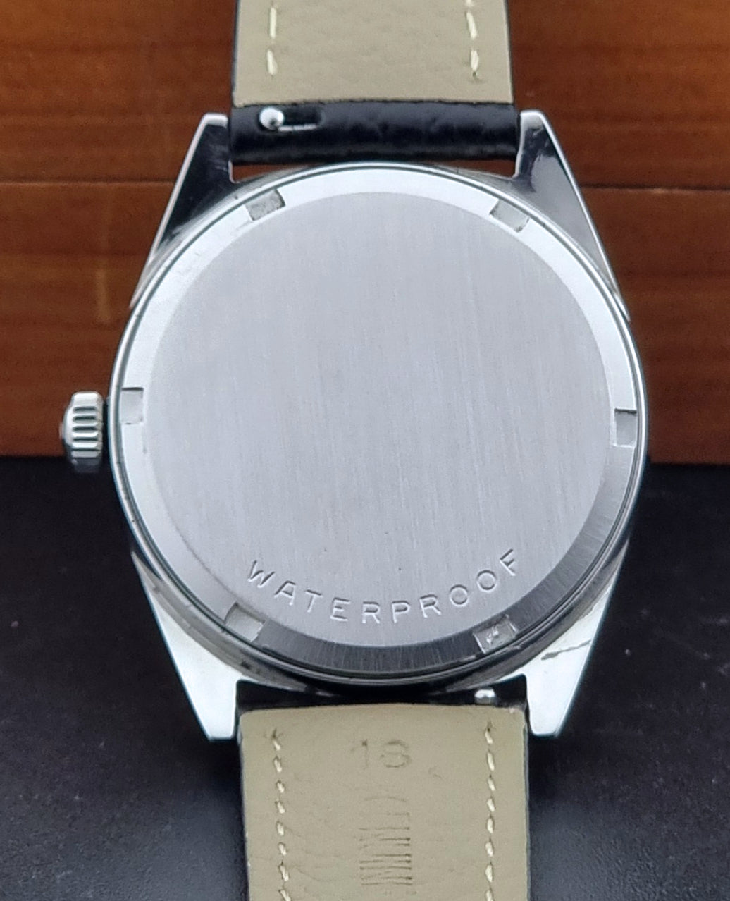 Vintage Omega watch Geneve 136.041 Co-signed Türler with a black leather strap and silver case on a dark background case back view