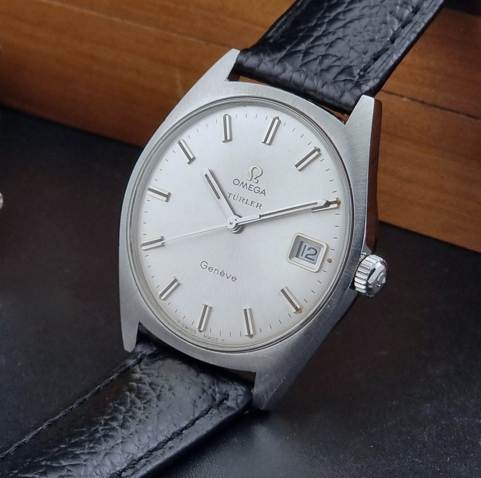 Vintage Omega watch Geneve 136.041 Co-signed Türler with a black leather strap and silver case on a dark background crown view