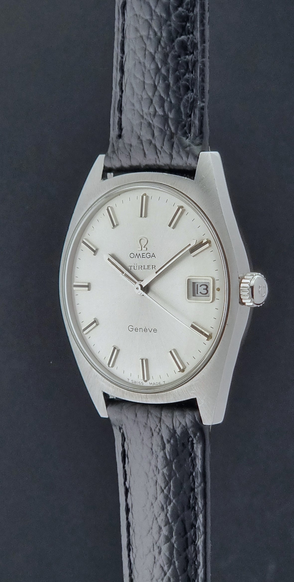 Vintage Omega watch Geneve 136.041 Co-signed Türler with a black leather strap and silver case on a dark background crown profile view