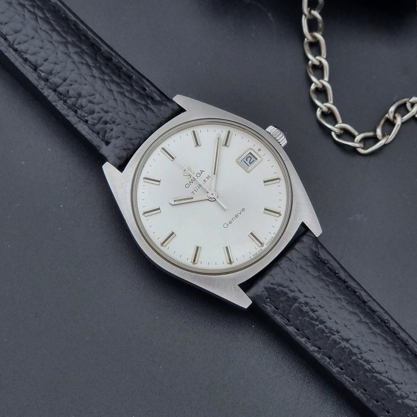 Vintage Omega watch Geneve 136.041 Co-signed Türler with a black leather strap and silver case on a dark background close up dial view