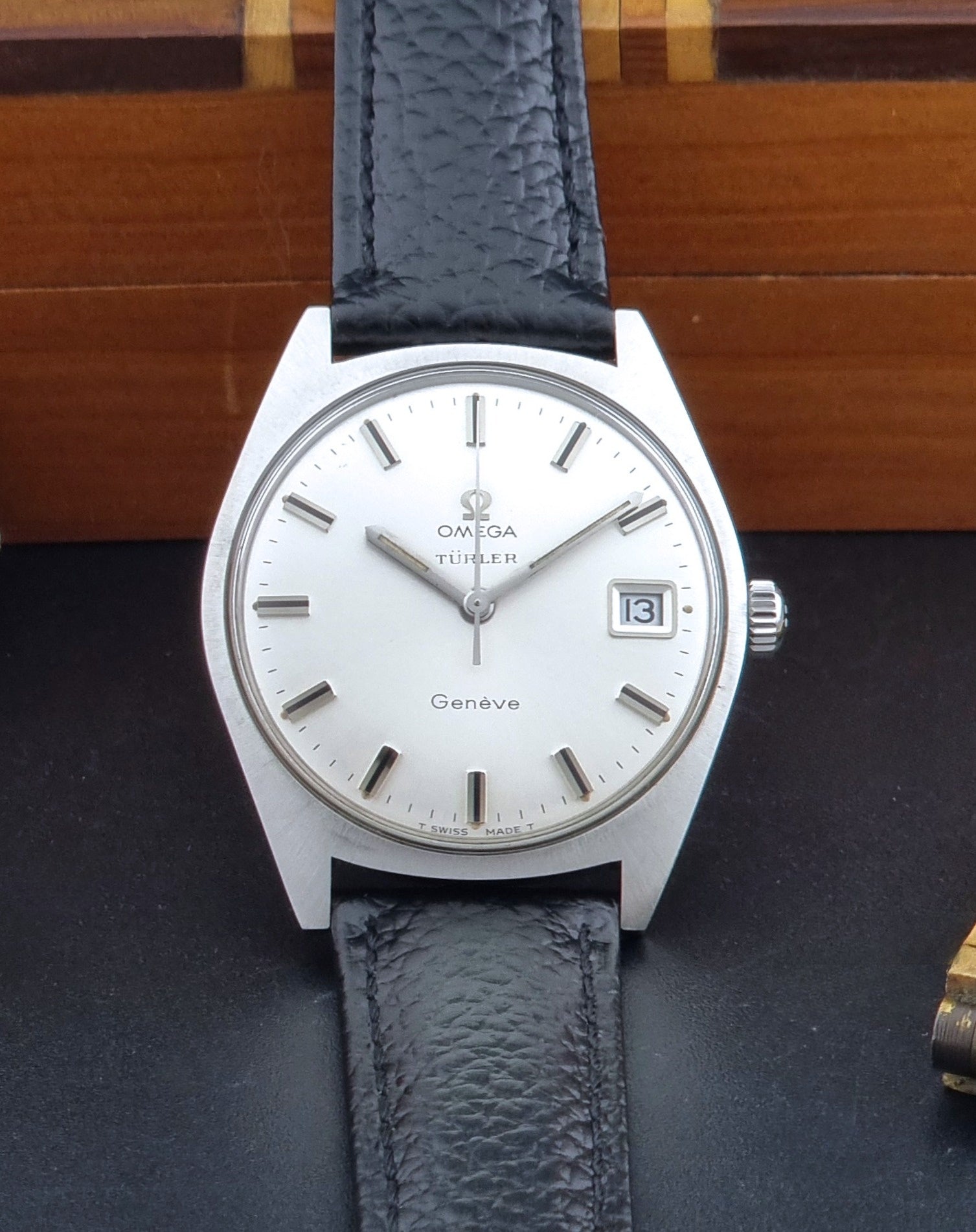Vintage Omega watch Geneve 136.041 Co-signed Türler with a black leather strap and silver case on a dark background dial view
